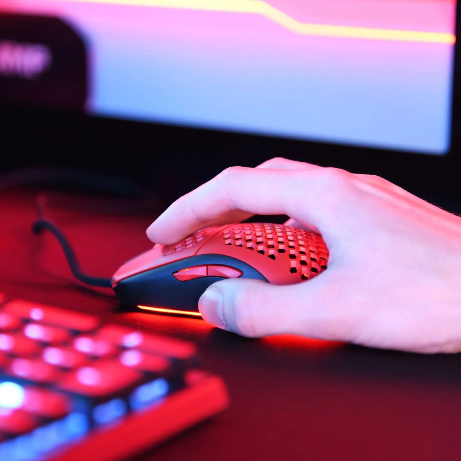 Rode gamingmuis met honingraatpatroon, vastgehouden door een hand, toetsenbord op voorgrond.