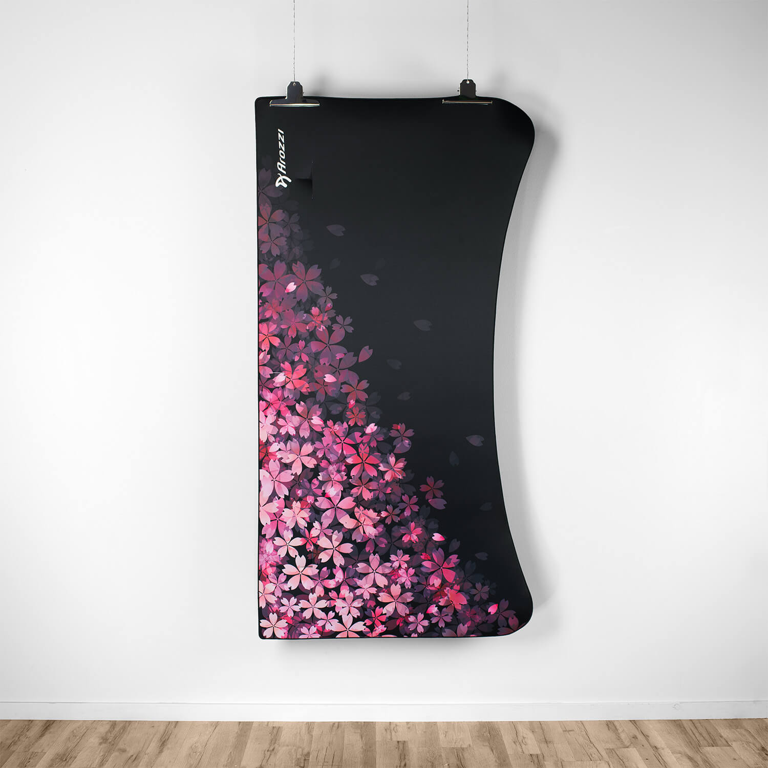 Een zwarte stof met roze kersenbloesems, hangend aan een witte muur.