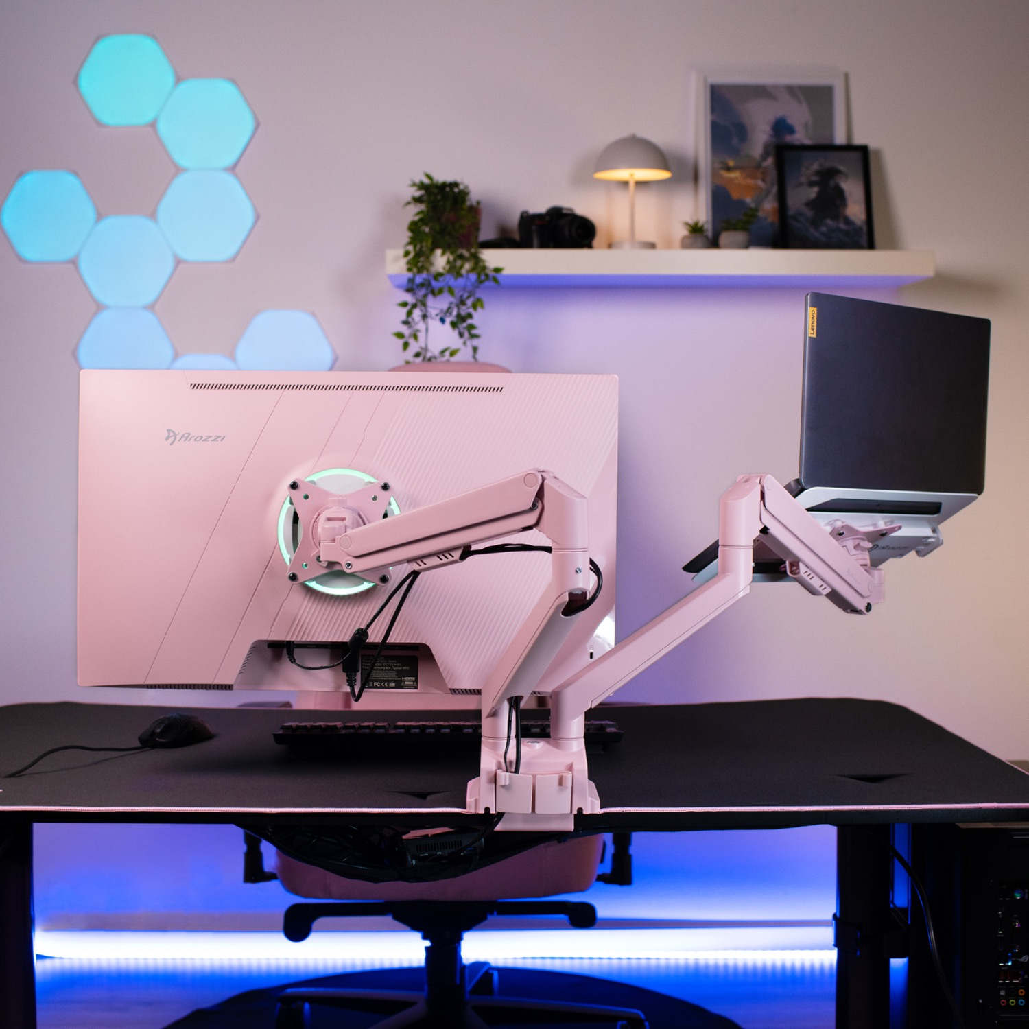 Een roze gaming-opstelling met dubbele monitoren op een armsteun en blauwe sfeerverlichting.