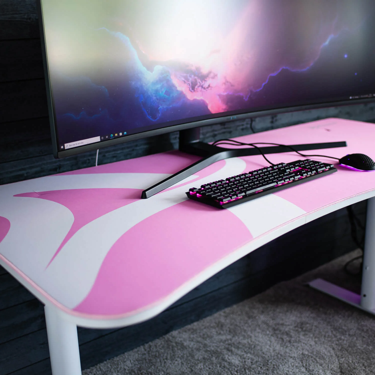 Ein Schreibtisch mit rosa Muster, Tastatur, Maus und einem Monitor mit Weltraum-Hintergrund.