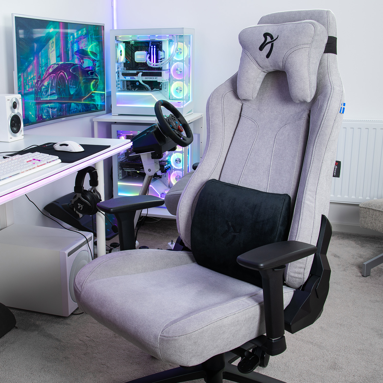 Una sedia da gaming grigia davanti a una scrivania con PC e luci al neon.