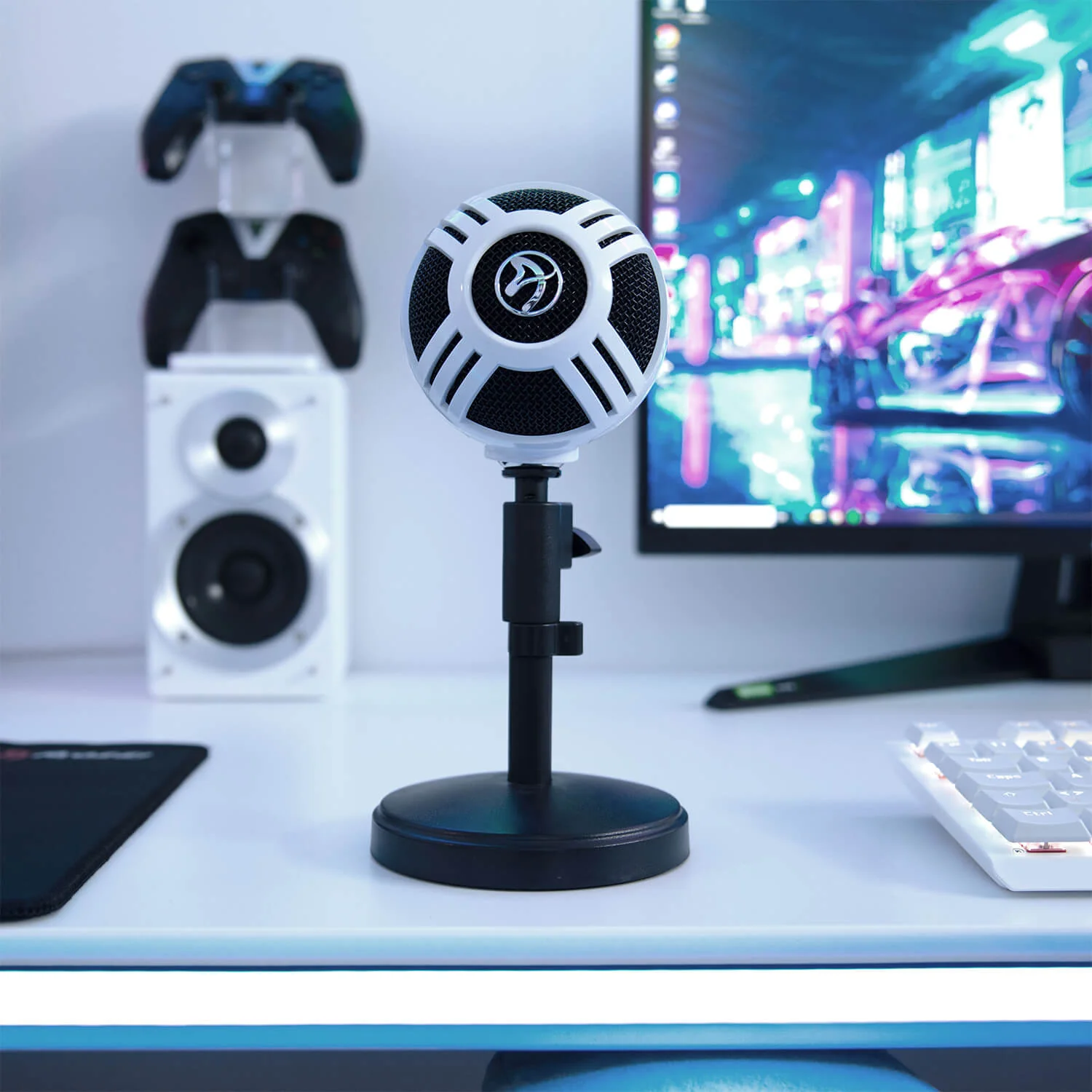 Een witte microfoon op een standaard, met controllers, luidspreker, toetsenbord en monitor.