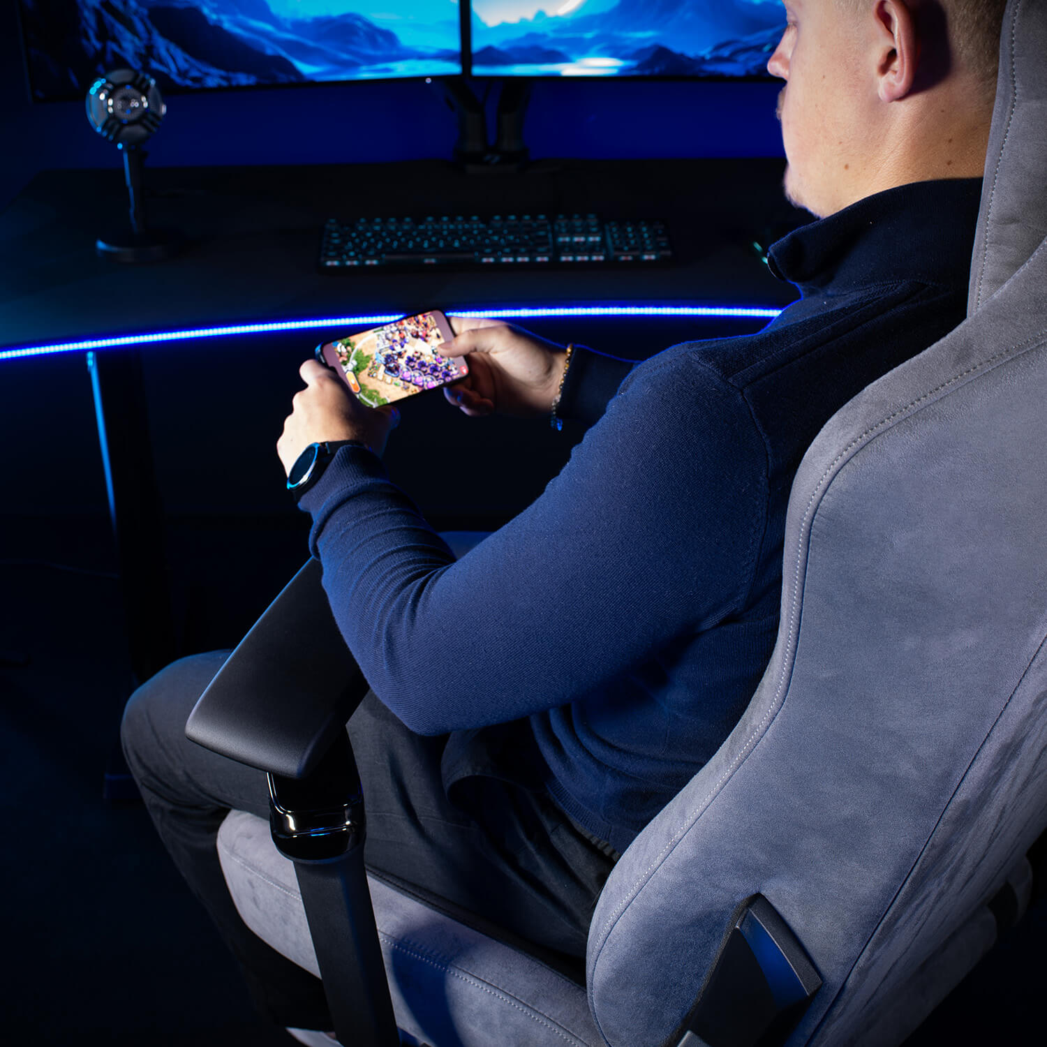 Un uomo siede su una sedia da gaming, giocando sul suo telefono tenuto orizzontalmente.