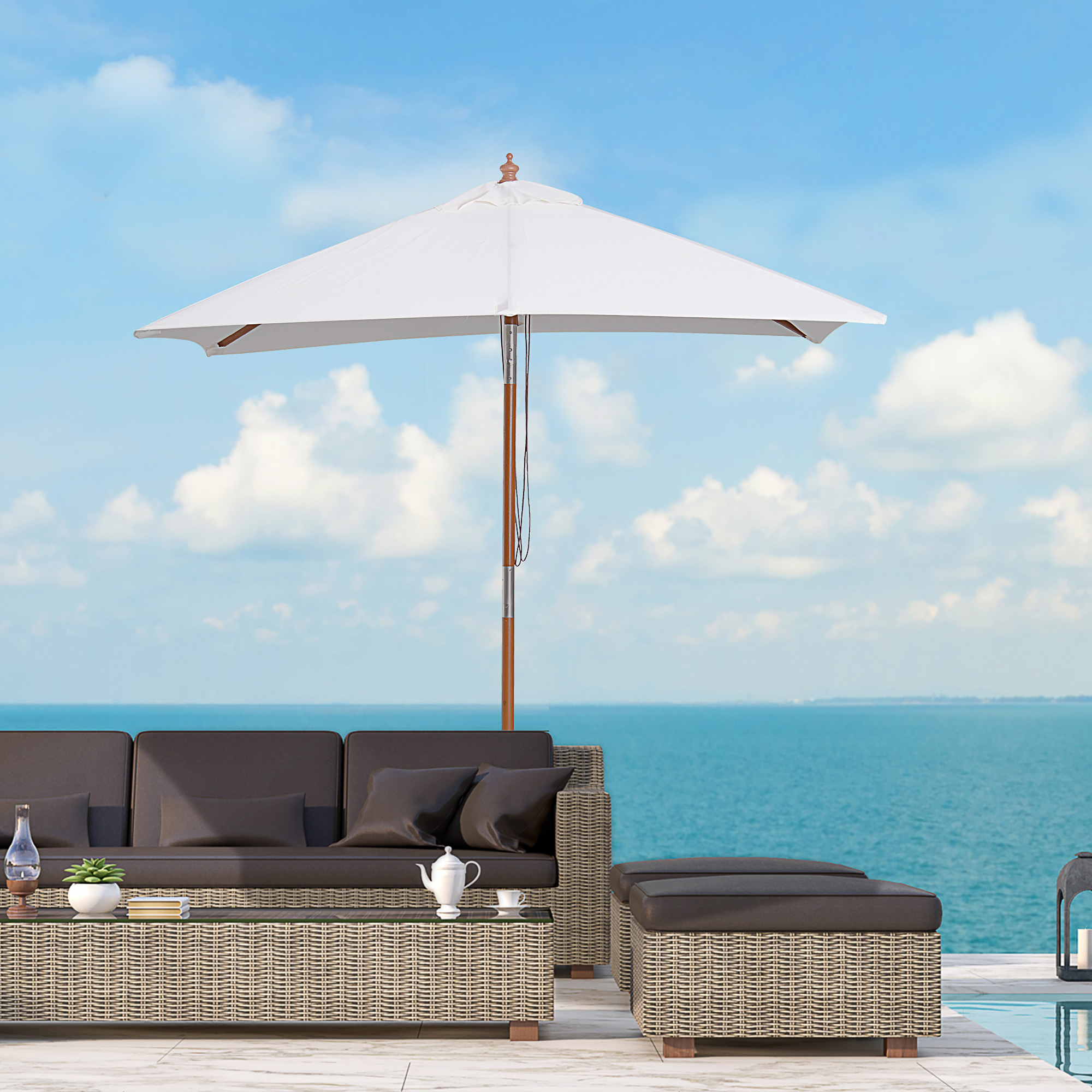 Set da salotto in vimini a bordo piscina con vista sul mare sotto un ombrellone.