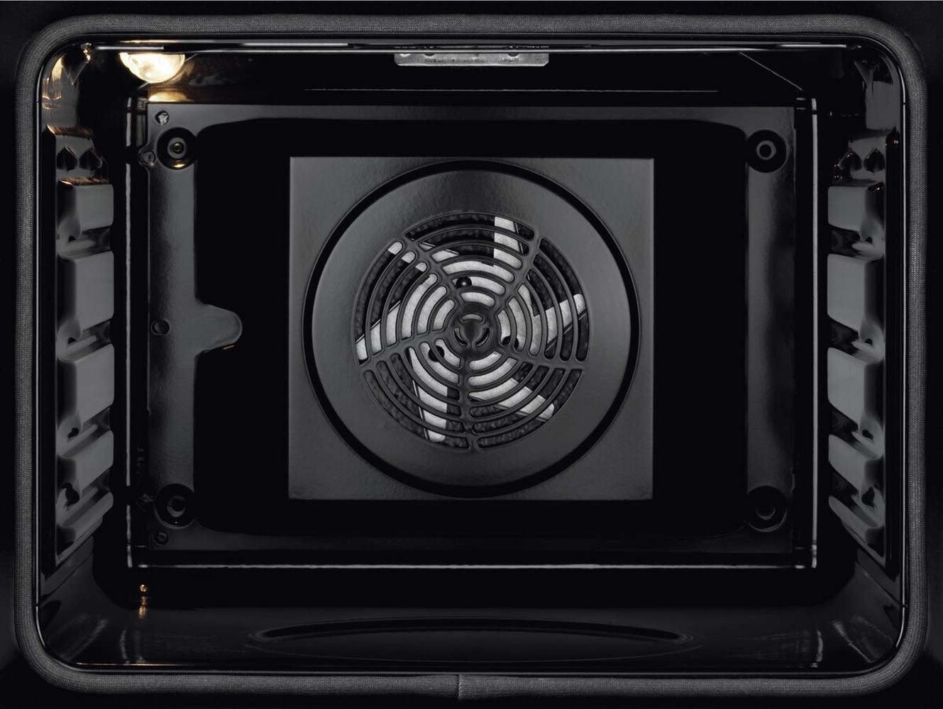Interno di un forno scuro con una griglia del ventilatore al centro.