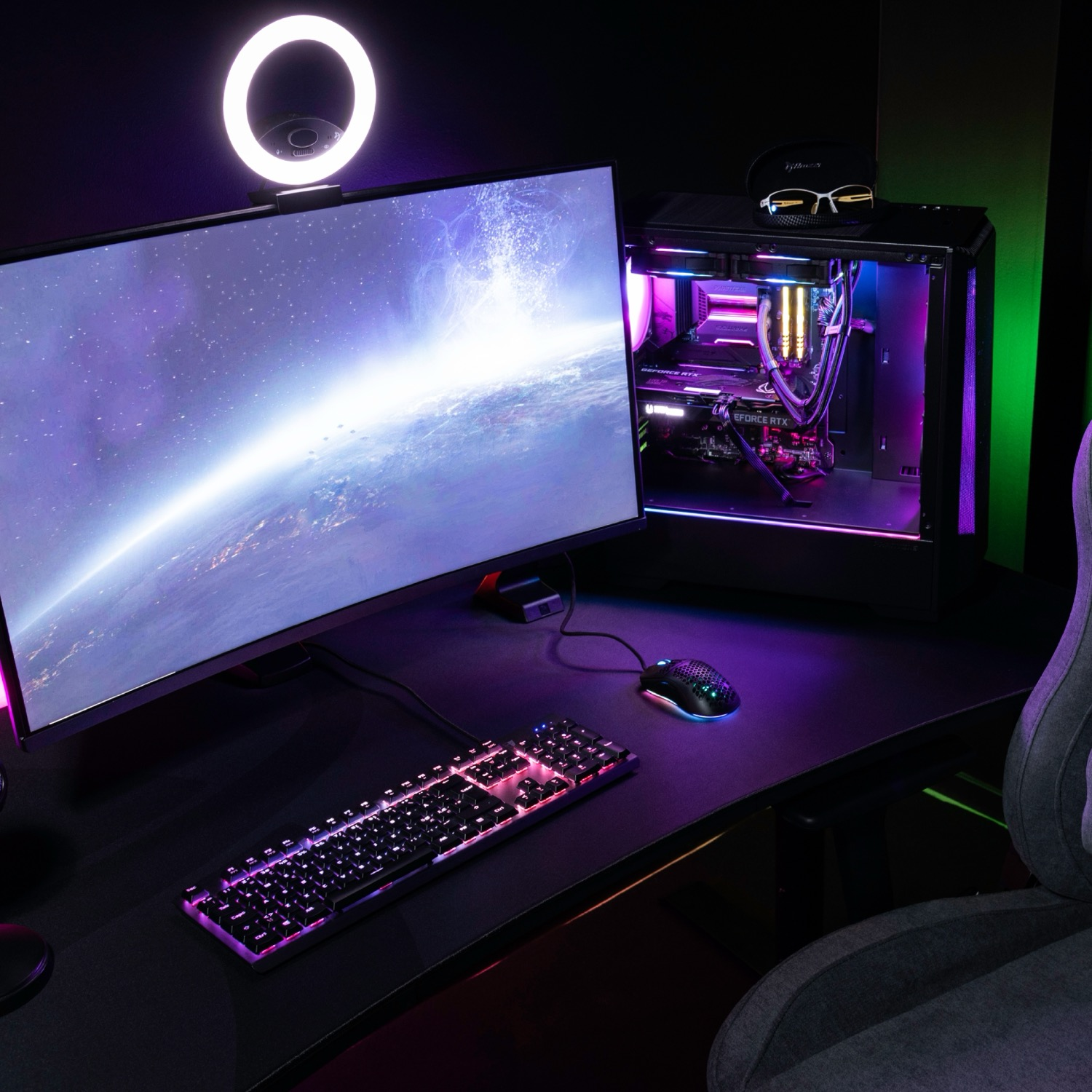 Een gaming-setup met pc, monitor die de aarde toont, toetsenbord, muis en ringlamp.