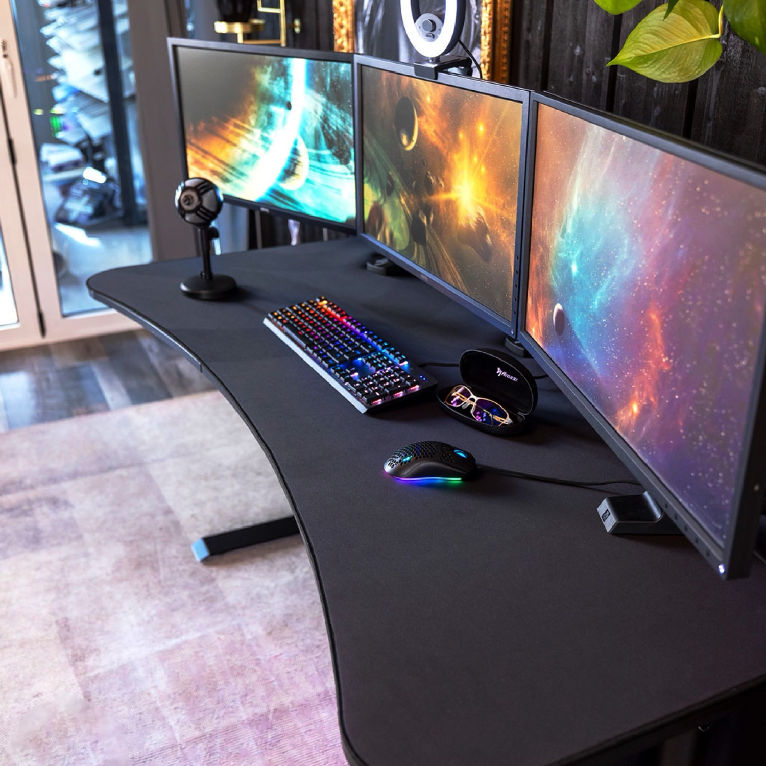 Een bureau met drie monitoren, toetsenbord, muis en microfoon.