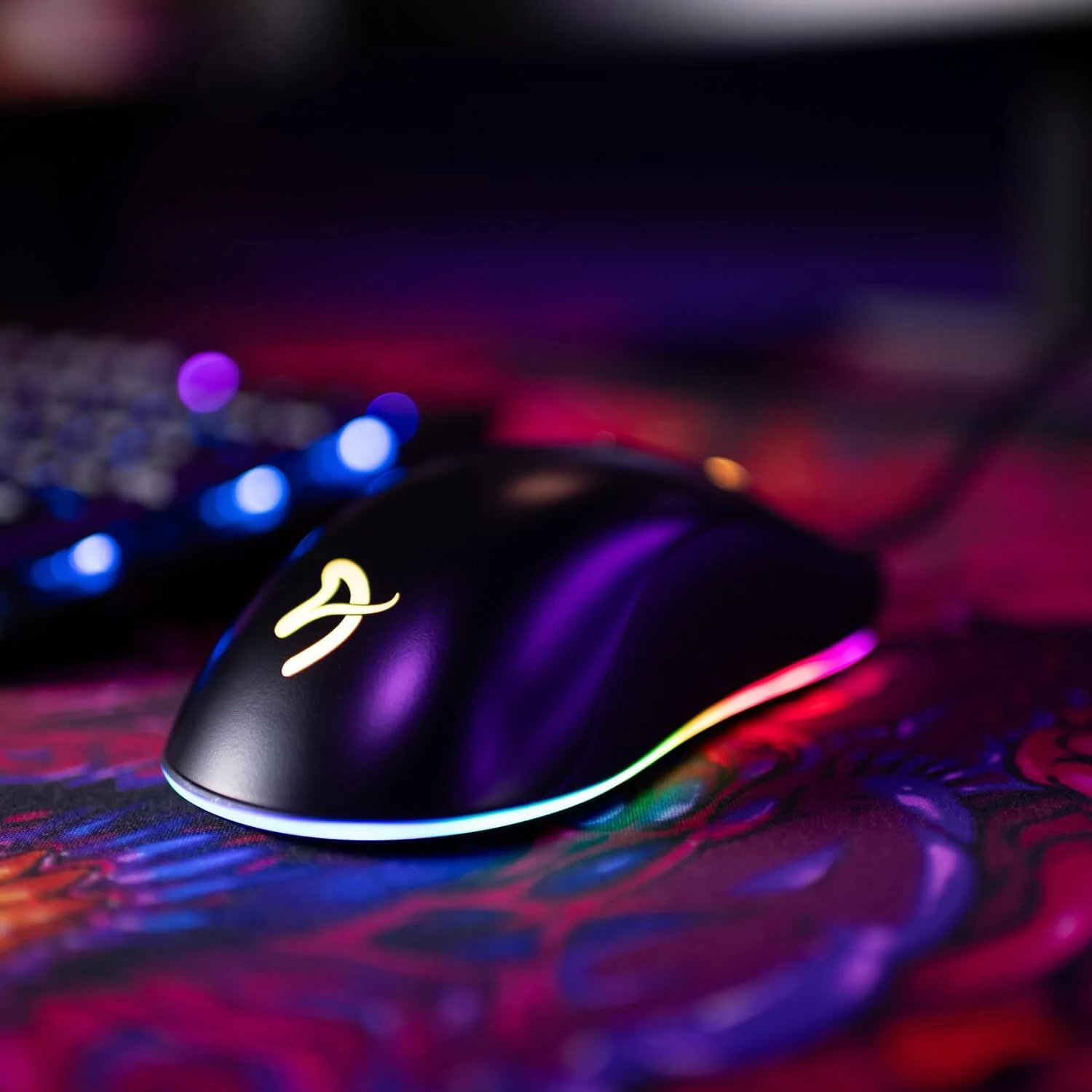 Een zwarte gamingmuis met een geel logo en RGB-verlichting op een kleurrijke mat.