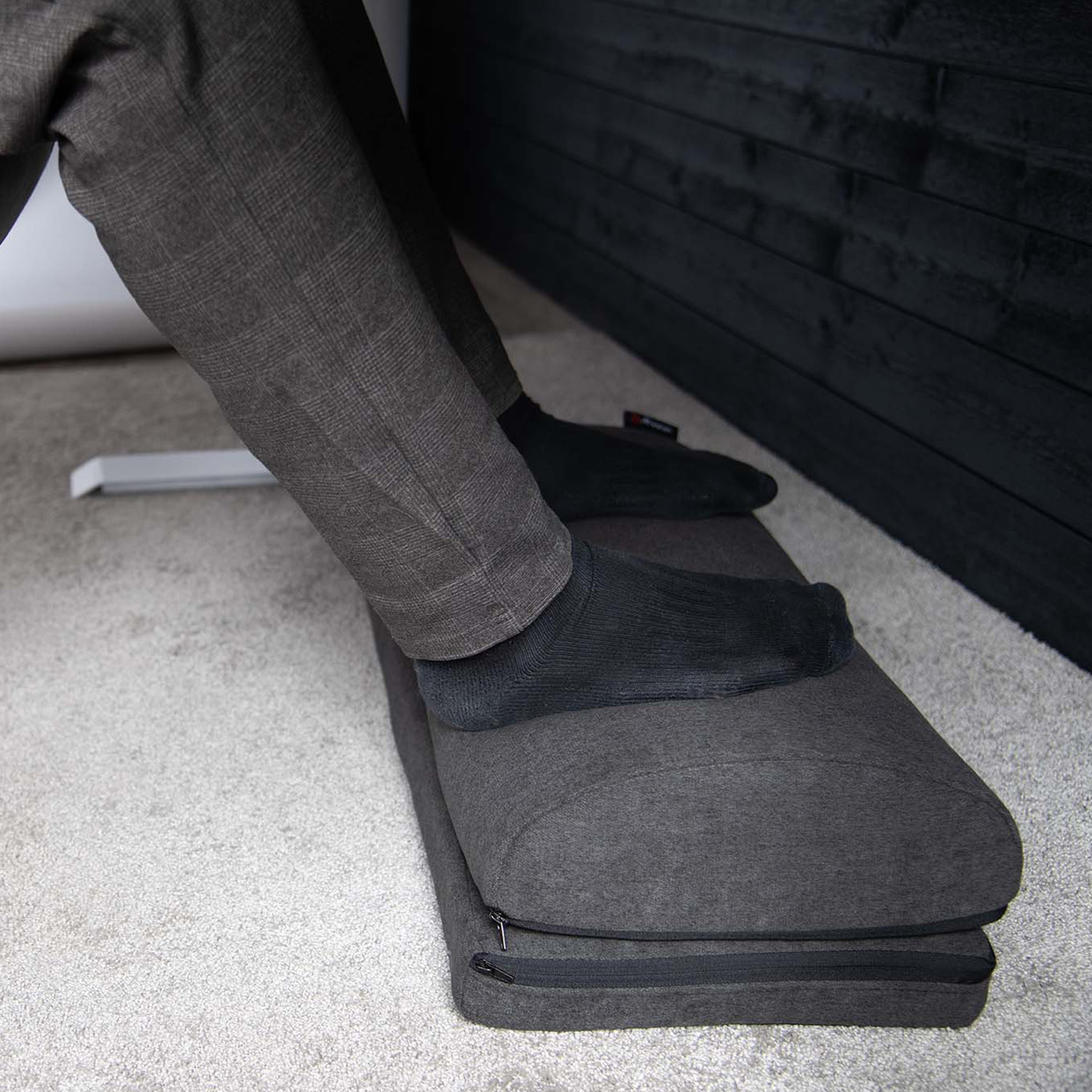 Una persona con pantaloni grigi e calzini neri appoggia i piedi su un poggiapiedi grigio.