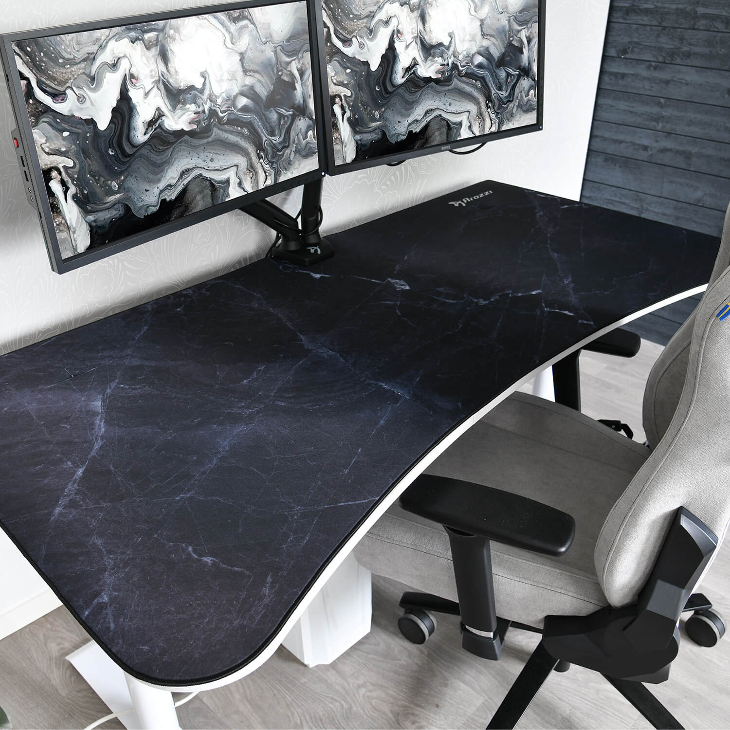 Een bureau met marmerpatroon, twee monitoren en een grijze stoel.
