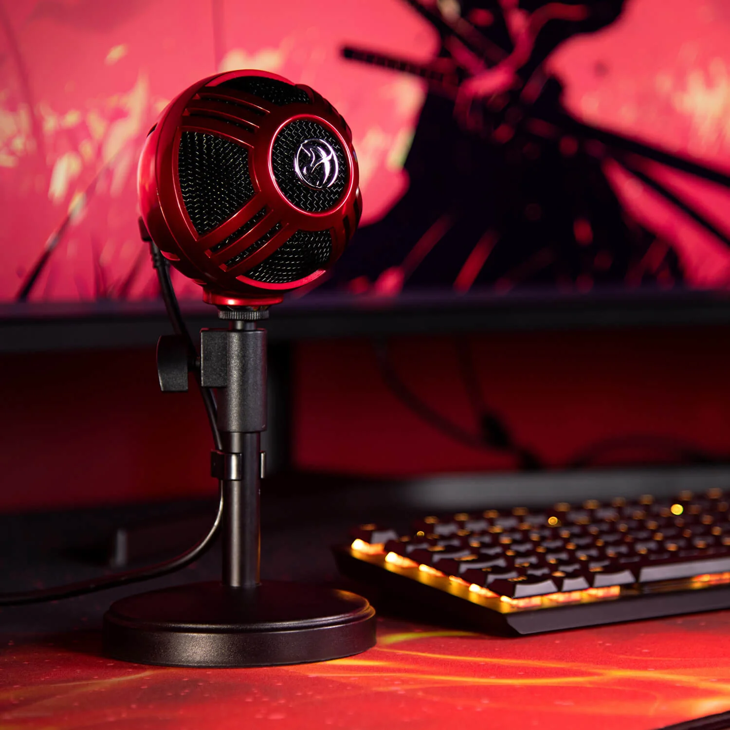Rode microfoon op standaard, gaming toetsenbord en monitor met rode achtergrond.