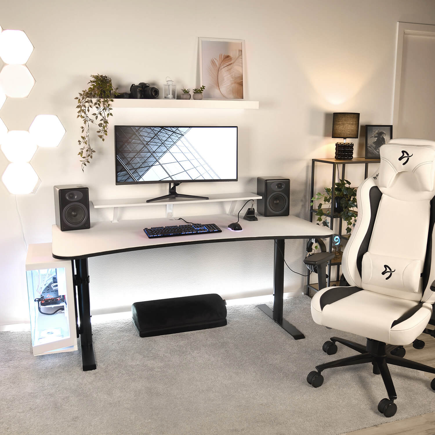 Una postazione da gaming con scrivania bianca, monitor, tastiera, altoparlanti e sedia bianca.