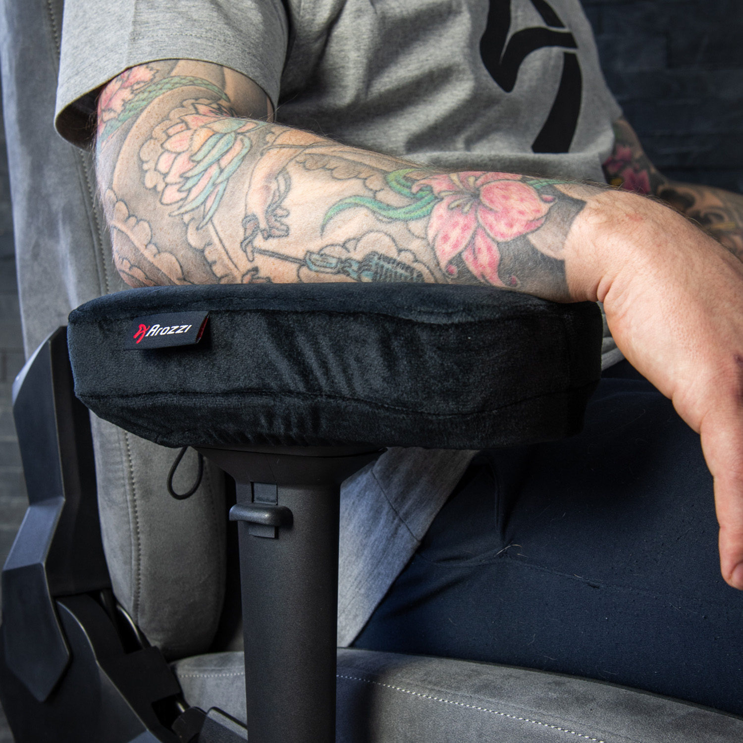 Man met getatoeëerde arm op stoel, armleuning met Arozzi-logo.