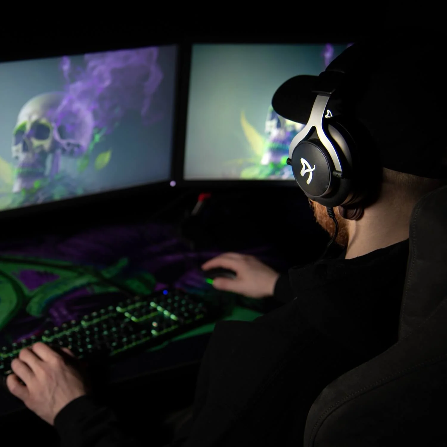 Gamer met koptelefoon speelt op toetsenbord en muis voor twee monitoren met schedels.