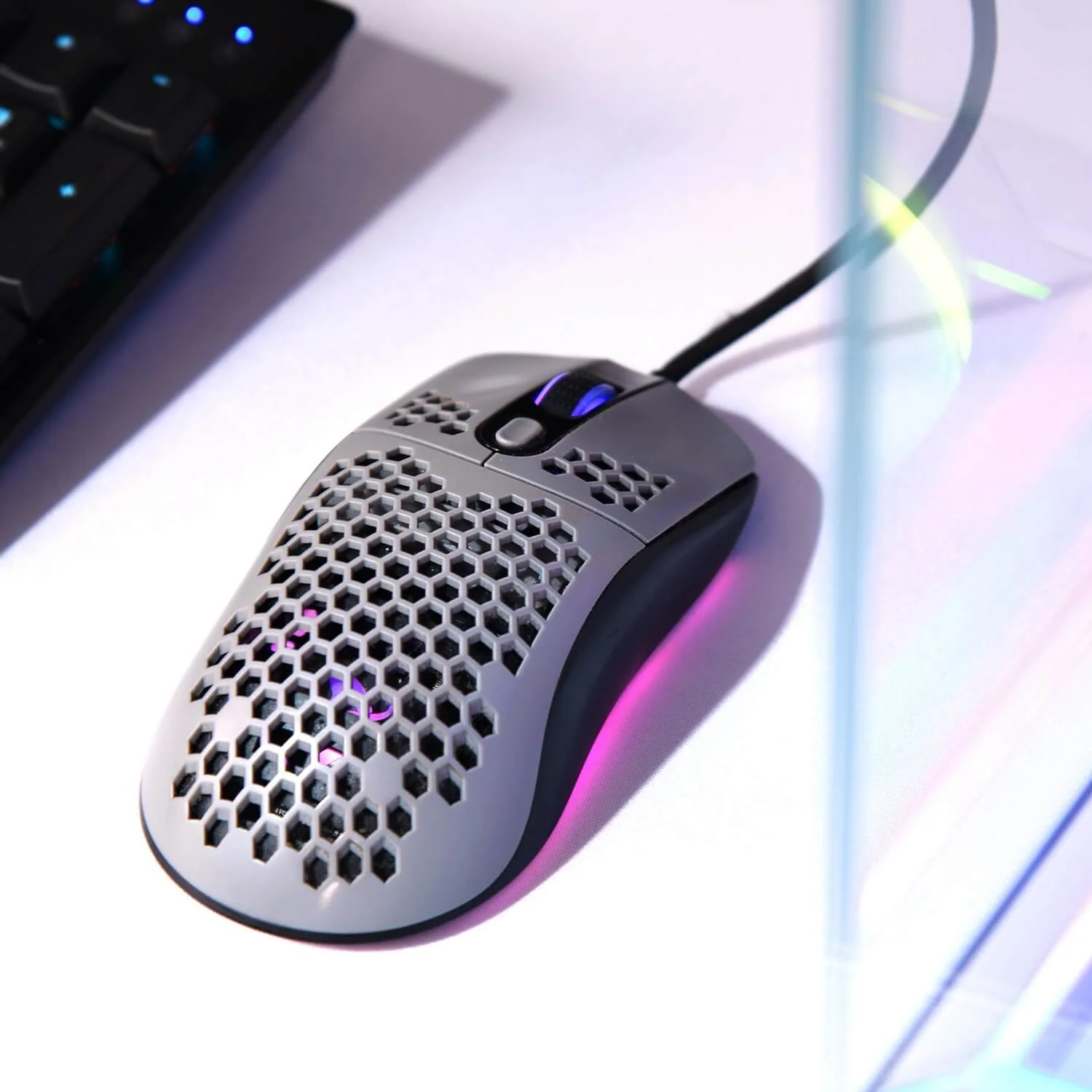 A gray honeycomb gaming mouse with RGB lighting sits next to a keyboard.