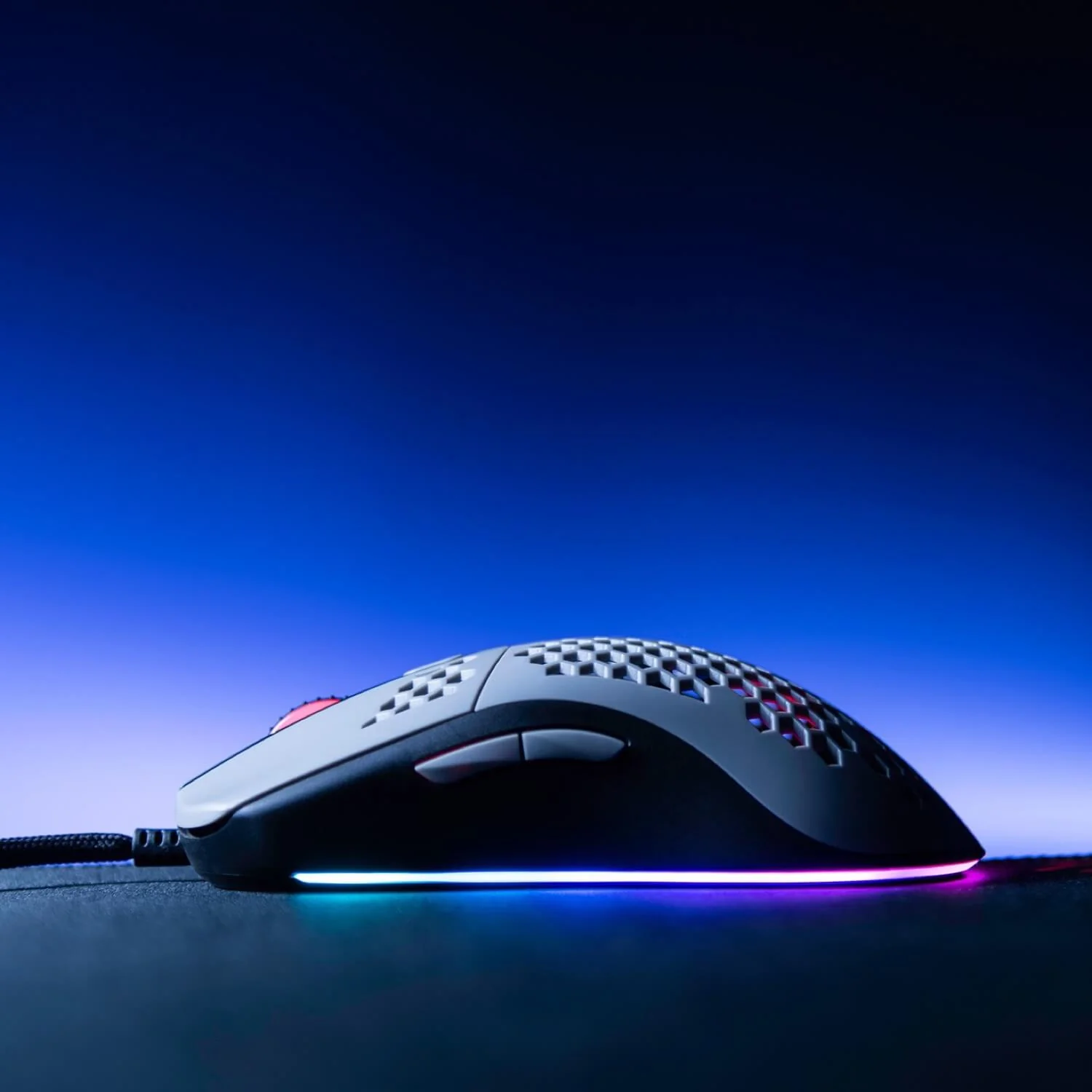 A white and black gaming mouse with RGB lighting sits on a dark surface.