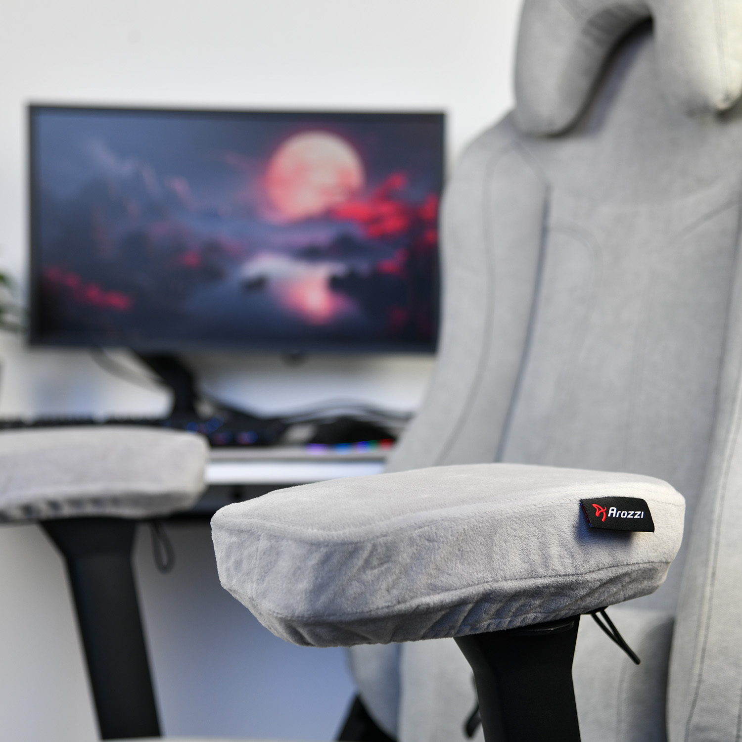Grijze gamestoel met armleuningen en Arozzi logo, monitor met maan op achtergrond.