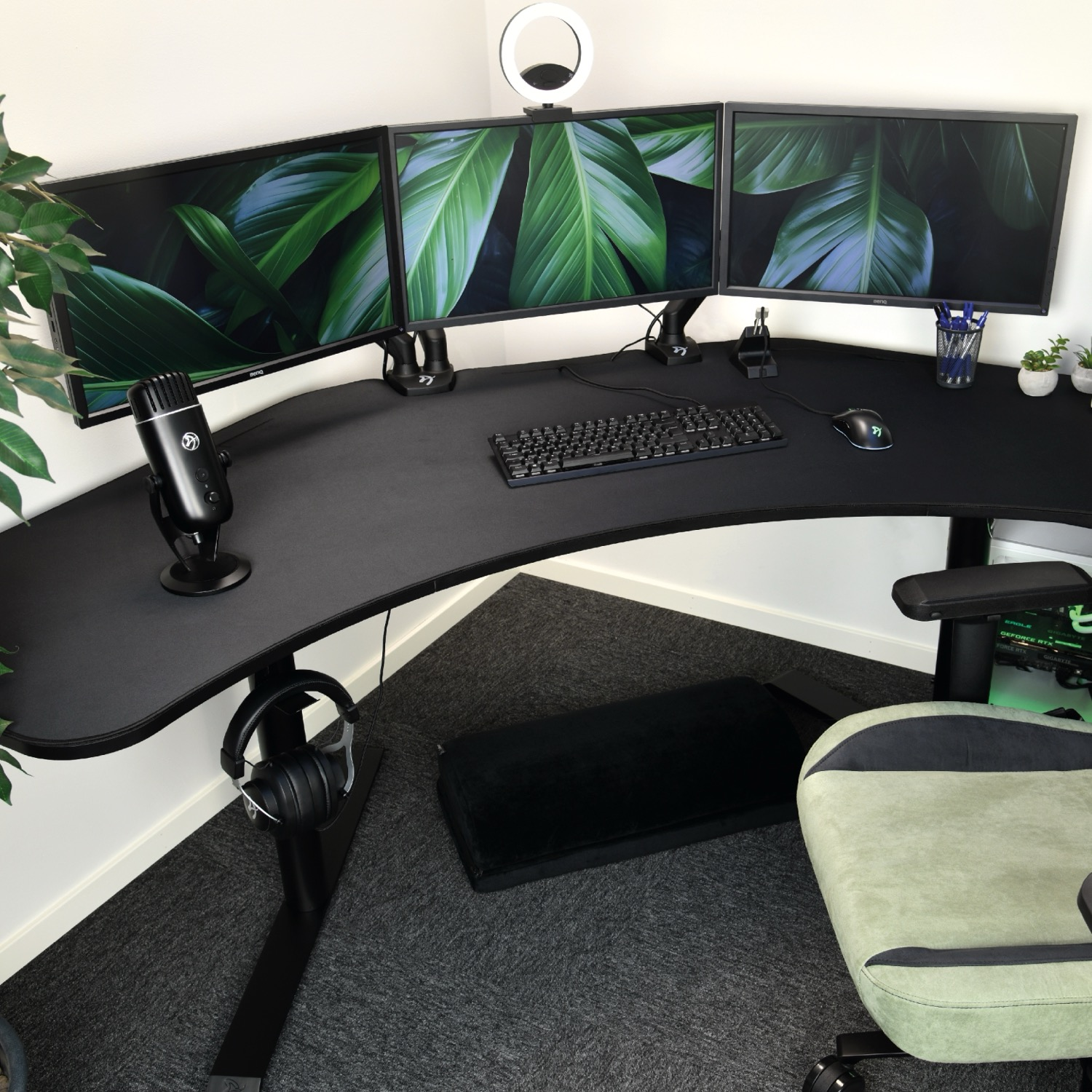 Una scrivania angolare con tre monitor, microfono, tastiera e mouse.