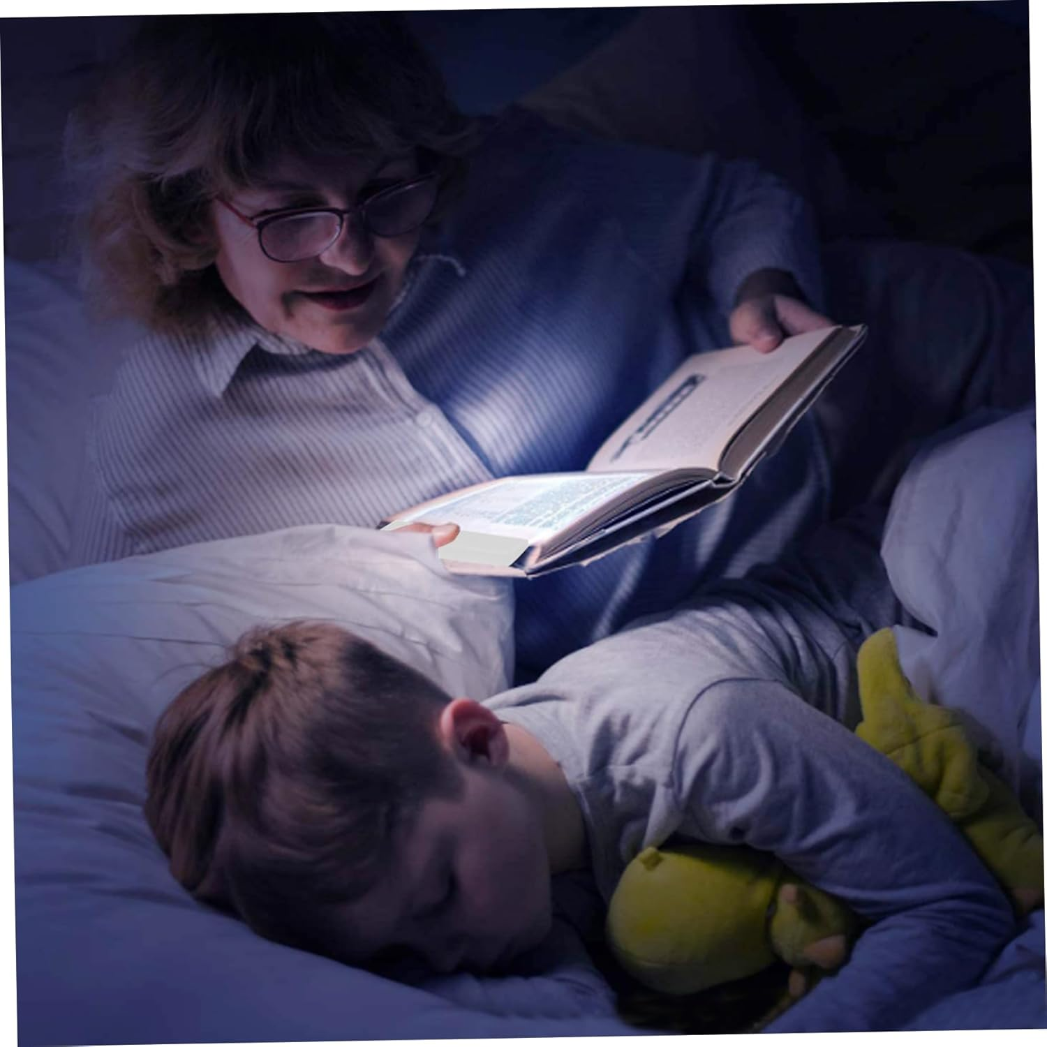Eine Frau liest einem schlafenden Jungen im Bett eine Geschichte vor. Ein Buch wird beleuchtet.