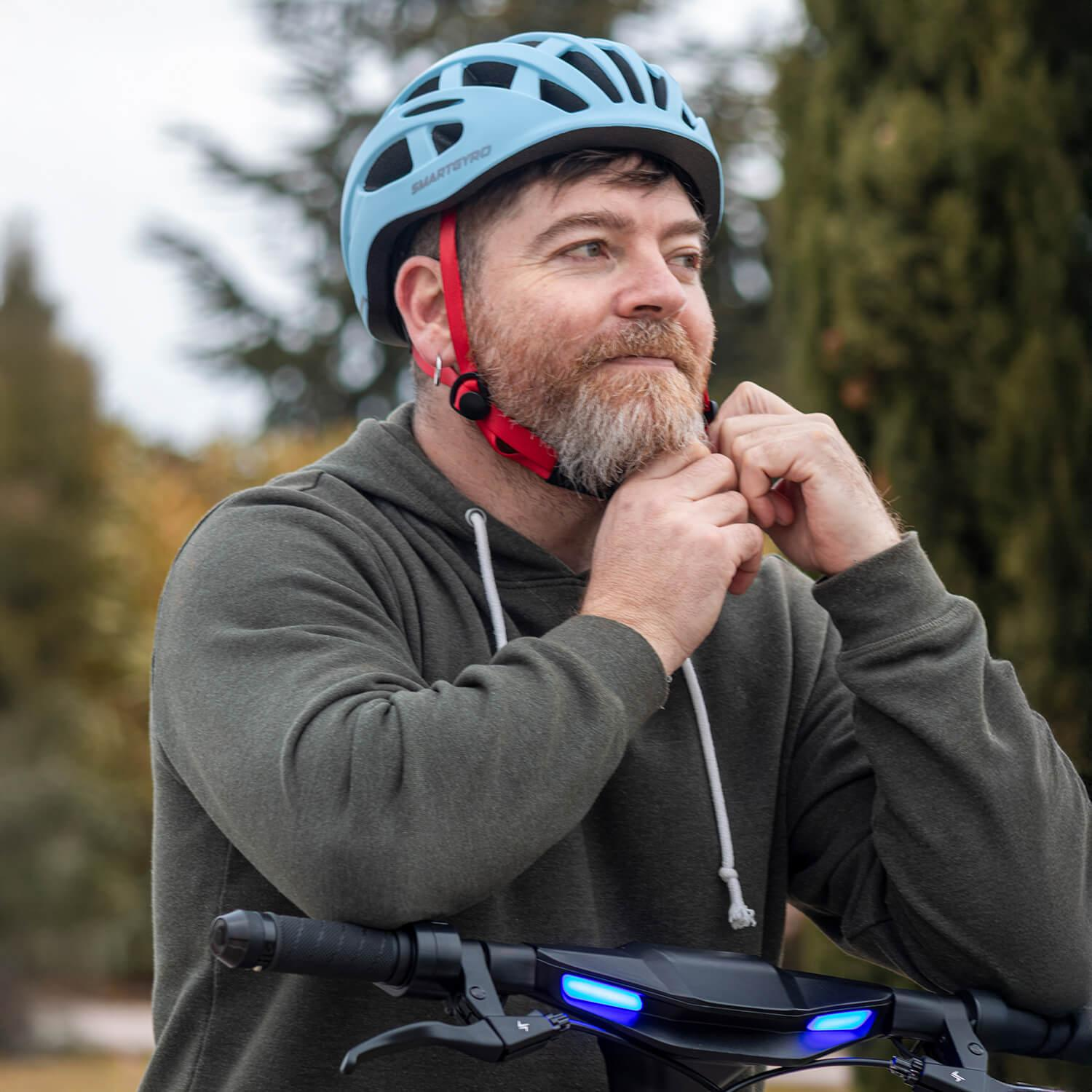 Hombre con barba ajusta casco azul, de pie en un patinete eléctrico.