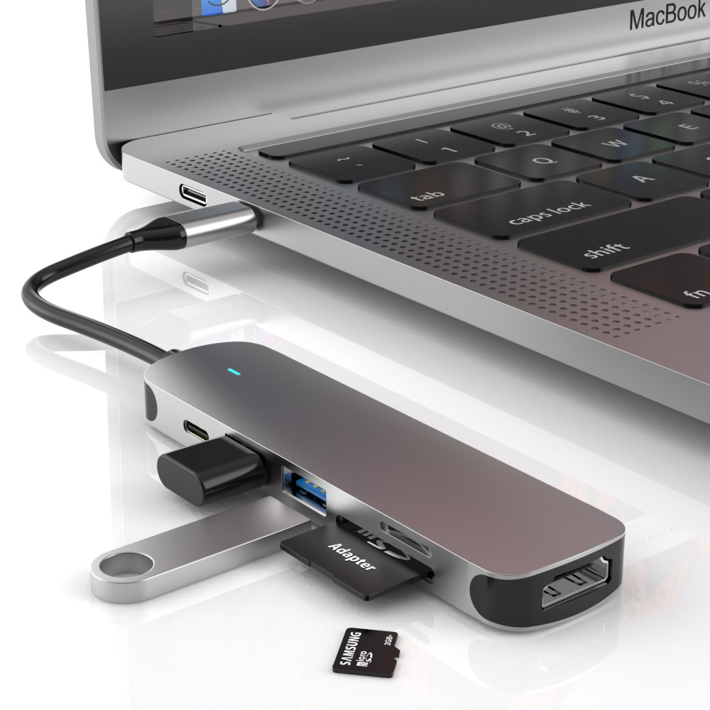 Un hub USB-C argento si collega a un MacBook, con slot per schede SD e porte USB visibili.