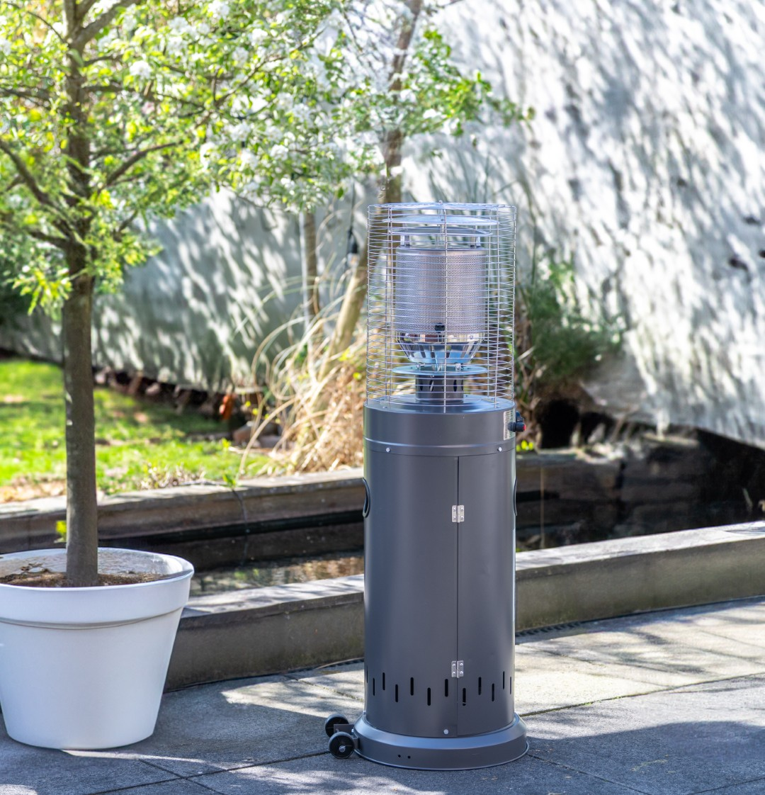 Grijze terrasverwarmer met wielen naast een boom in een witte pot.