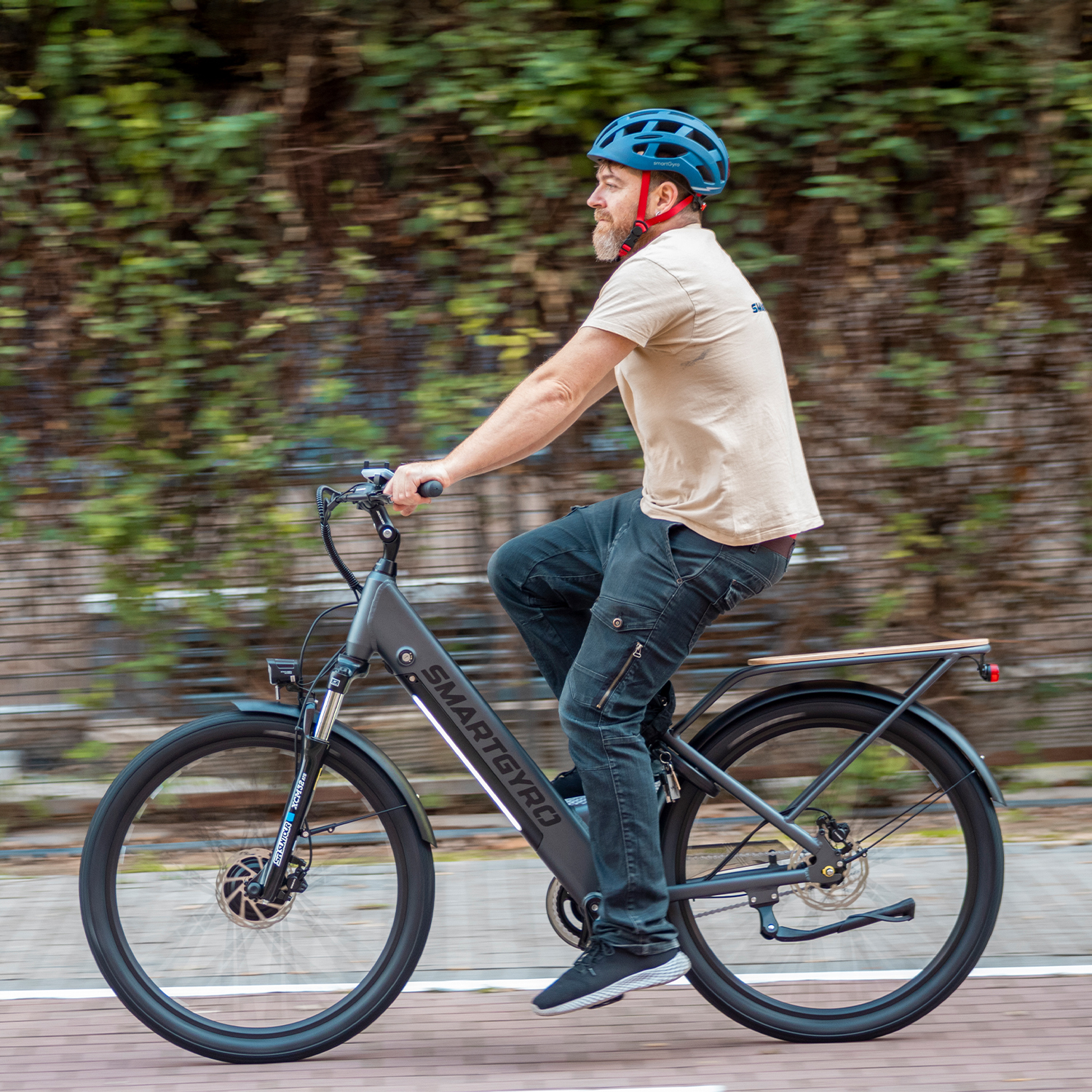 Hombre con casco azul monta una e-bike SmartGyro gris sobre superficie de madera.