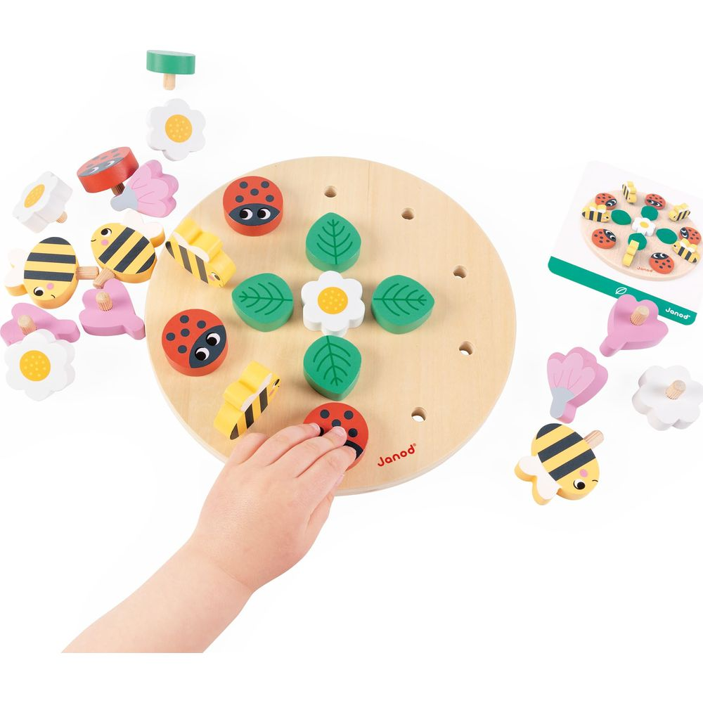 La mano di un bambino posiziona una coccinella su una tavola di legno con pezzi di fiori, foglie e api.