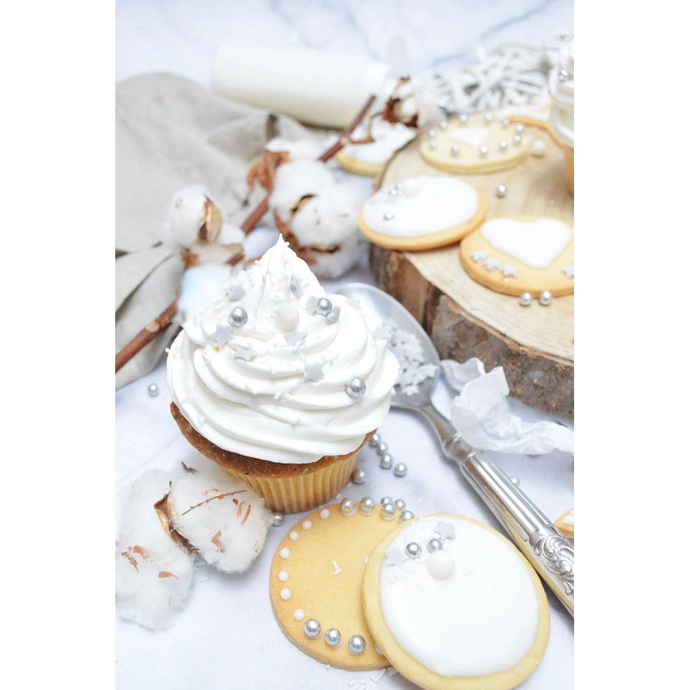Ein Cupcake mit weißer Glasur, bestreut mit silbernen Perlen, neben Keksen.