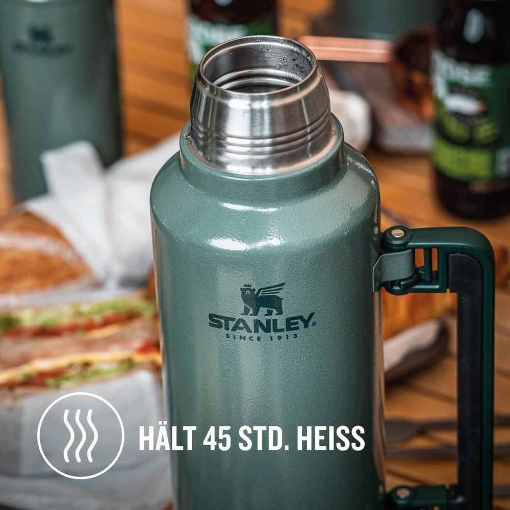 Termo verde Stanley con asa, al lado de sándwiches y botellas.