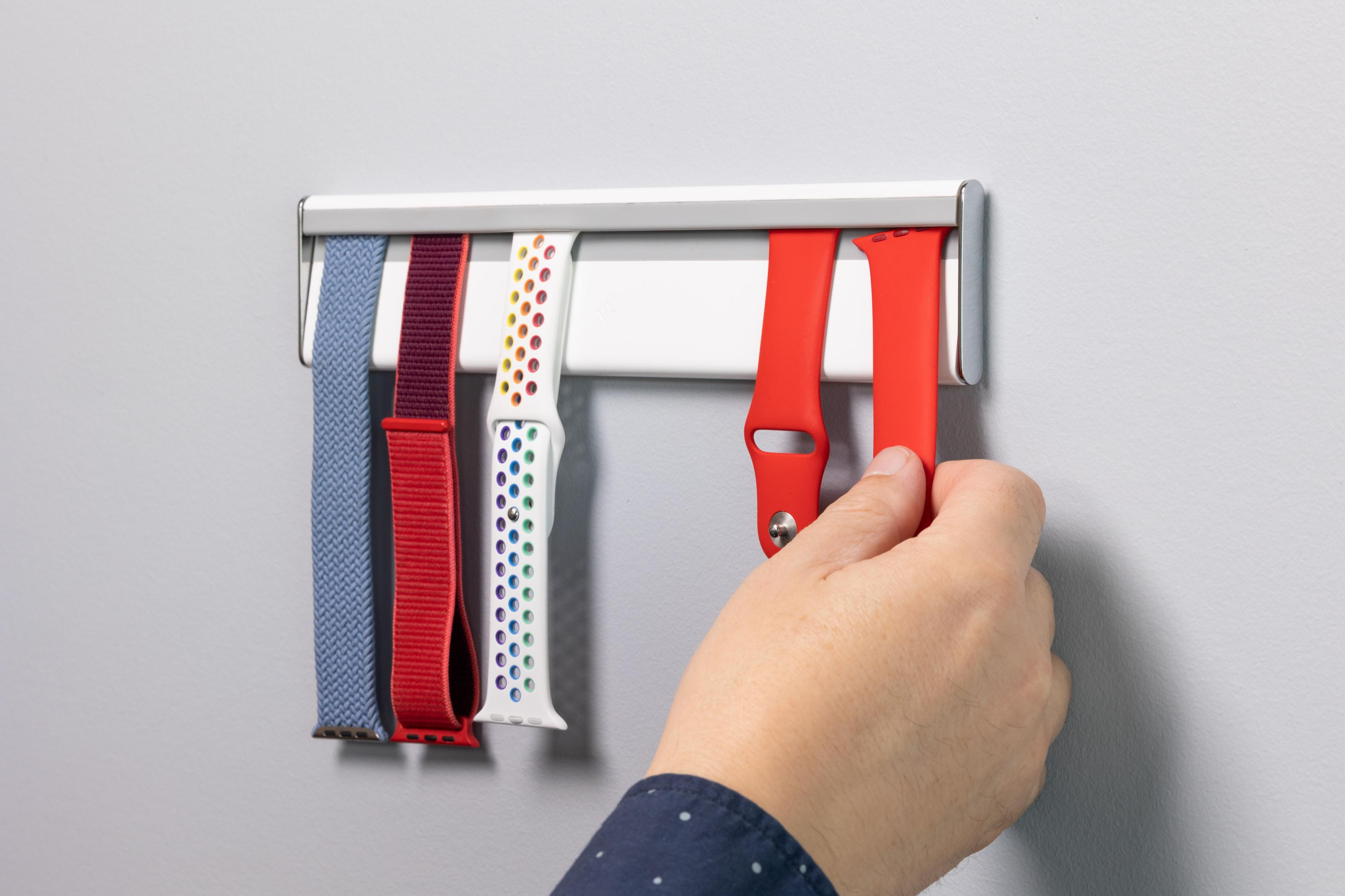 Eine Hand entfernt ein rotes Uhrenarmband aus einem weißen Halter mit anderen Bändern.