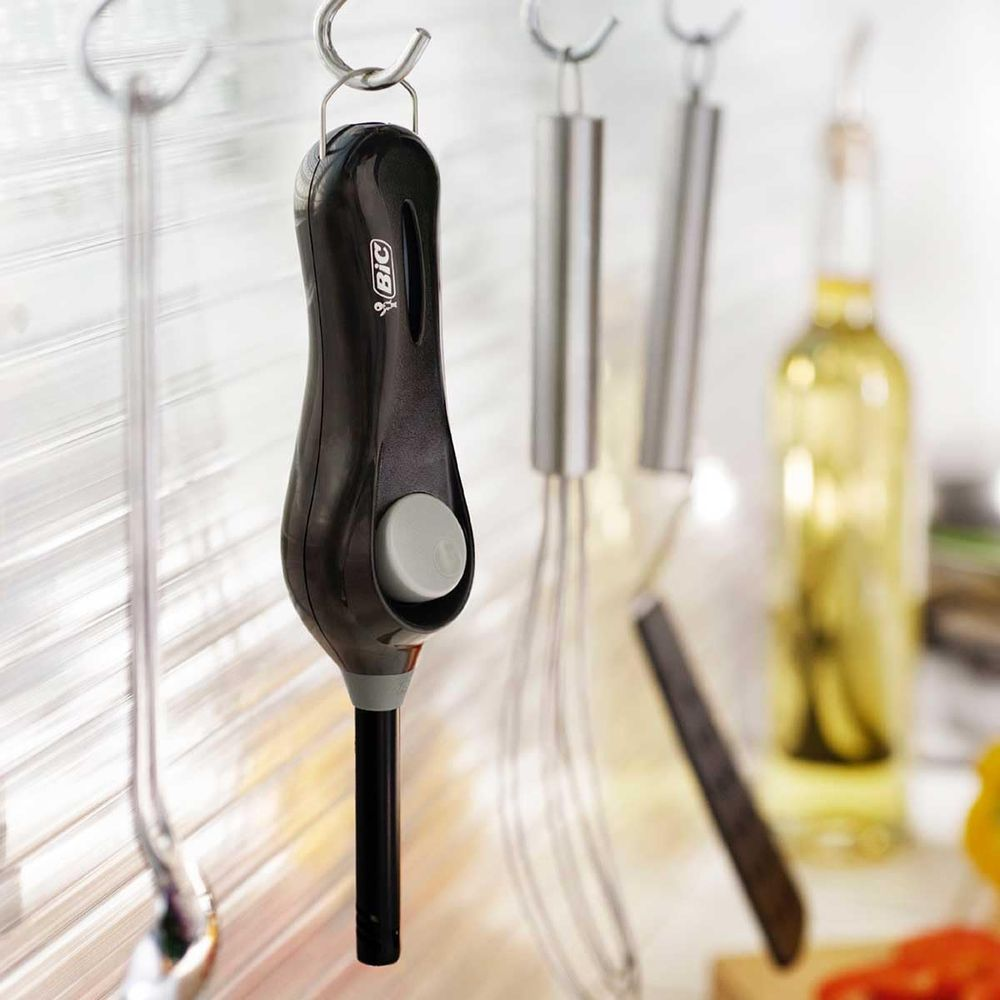 Accendino da cucina nero con pulsante grigio appeso a un gancio. accanto c'è una frusta.