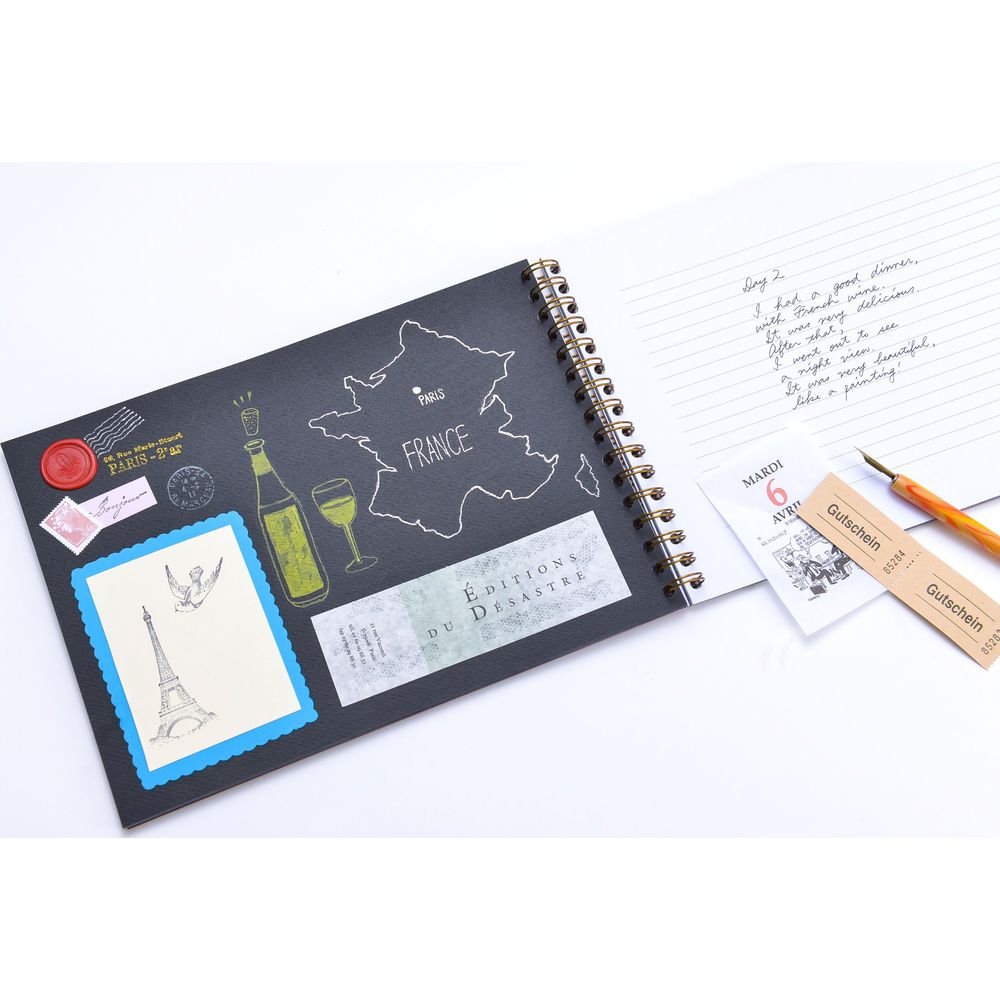 Ein Notizbuch mit Frankreich-Motiv, Wein, Eiffelturm-Aufkleber und handschriftlichem Tagebucheintrag.