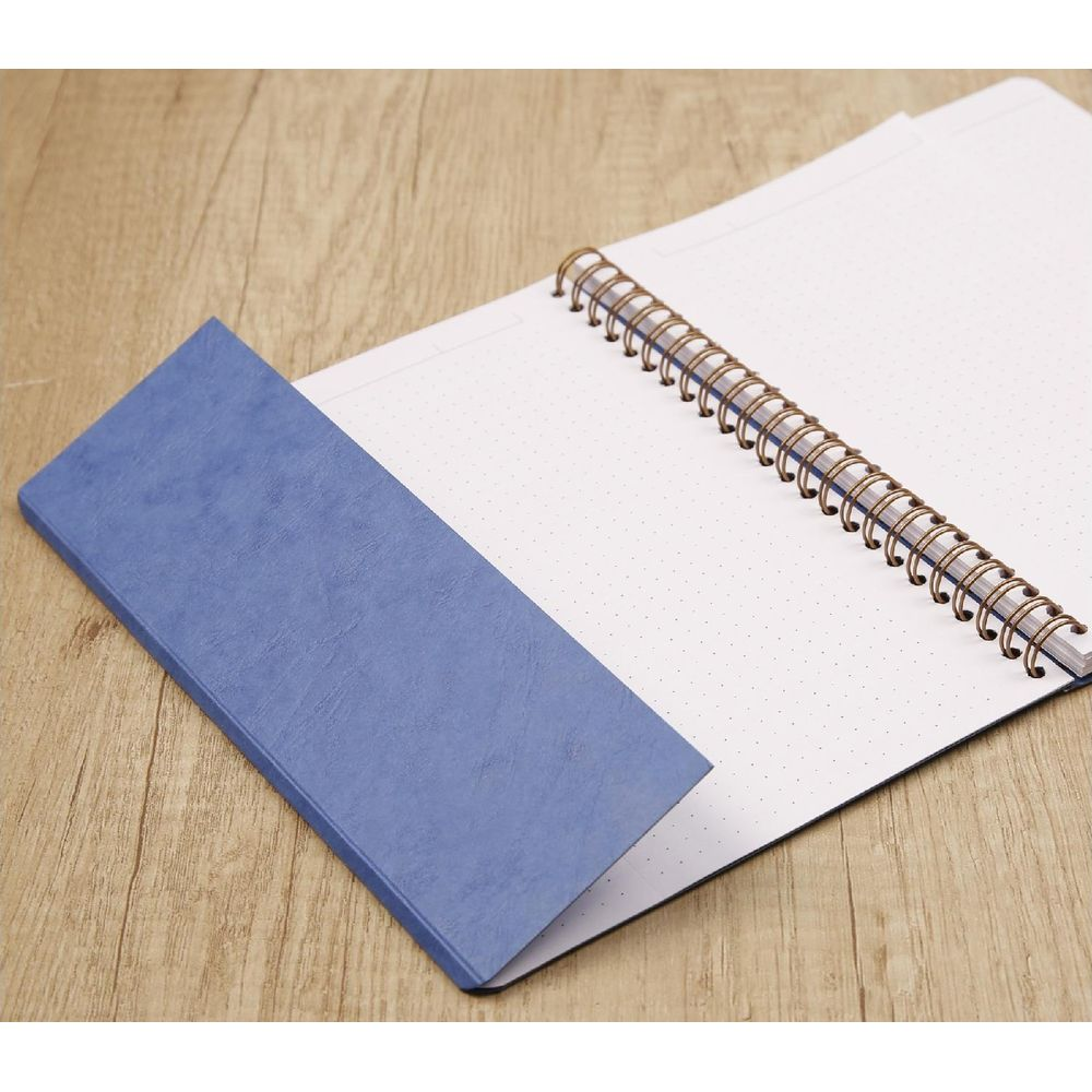 Ein blau gebundenes Notizbuch liegt offen auf einem Holztisch und zeigt gepunktete Seiten.