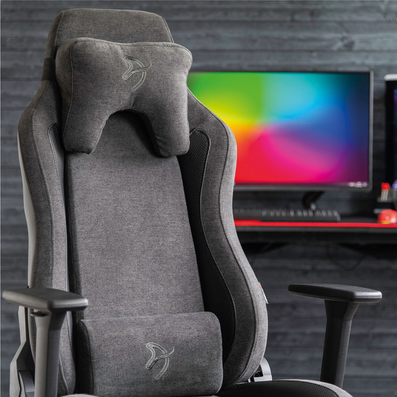 Una sedia da gaming grigia con poggiatesta e cuscino lombare si trova davanti a un monitor con sfumatura di colore.