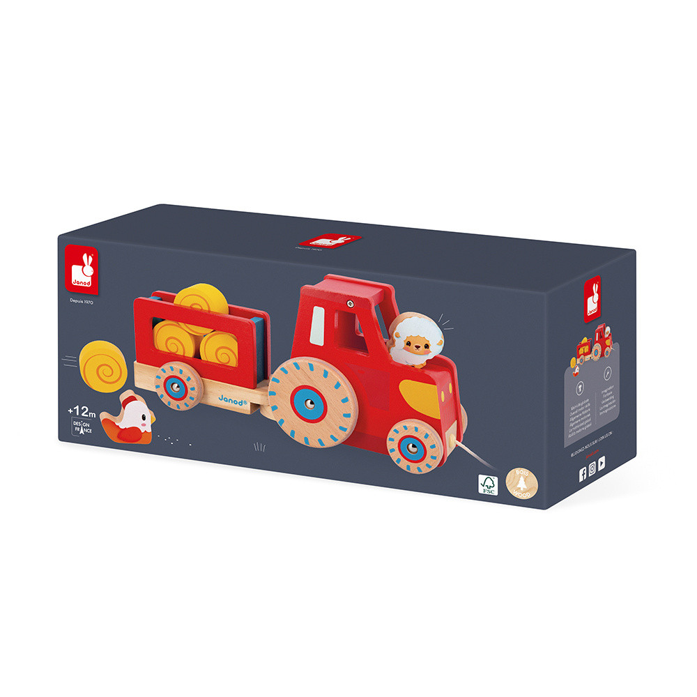 Roter Holz-Spielzeugtraktor mit Anhänger, Heuballen und Tierfiguren auf dunkler Verpackung.