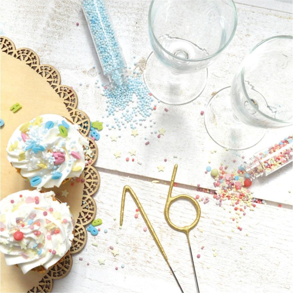 Zwei Cupcakes mit weißem Zuckerguss und Streuseln, goldene Zahlenkerzen, Gläser und verstreute Streusel.