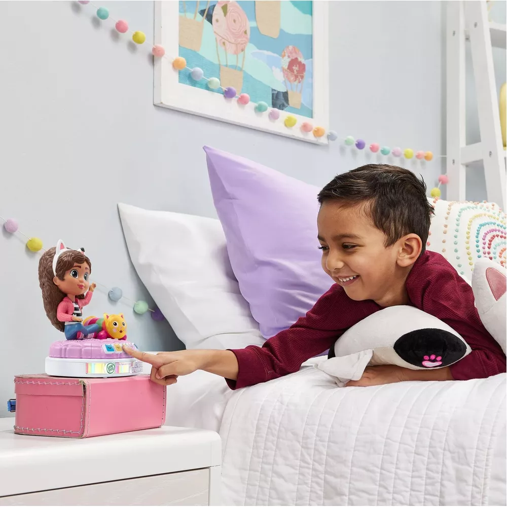 Un bambino è sdraiato su un letto, interagisce con una figura giocattolo su una base luminosa.