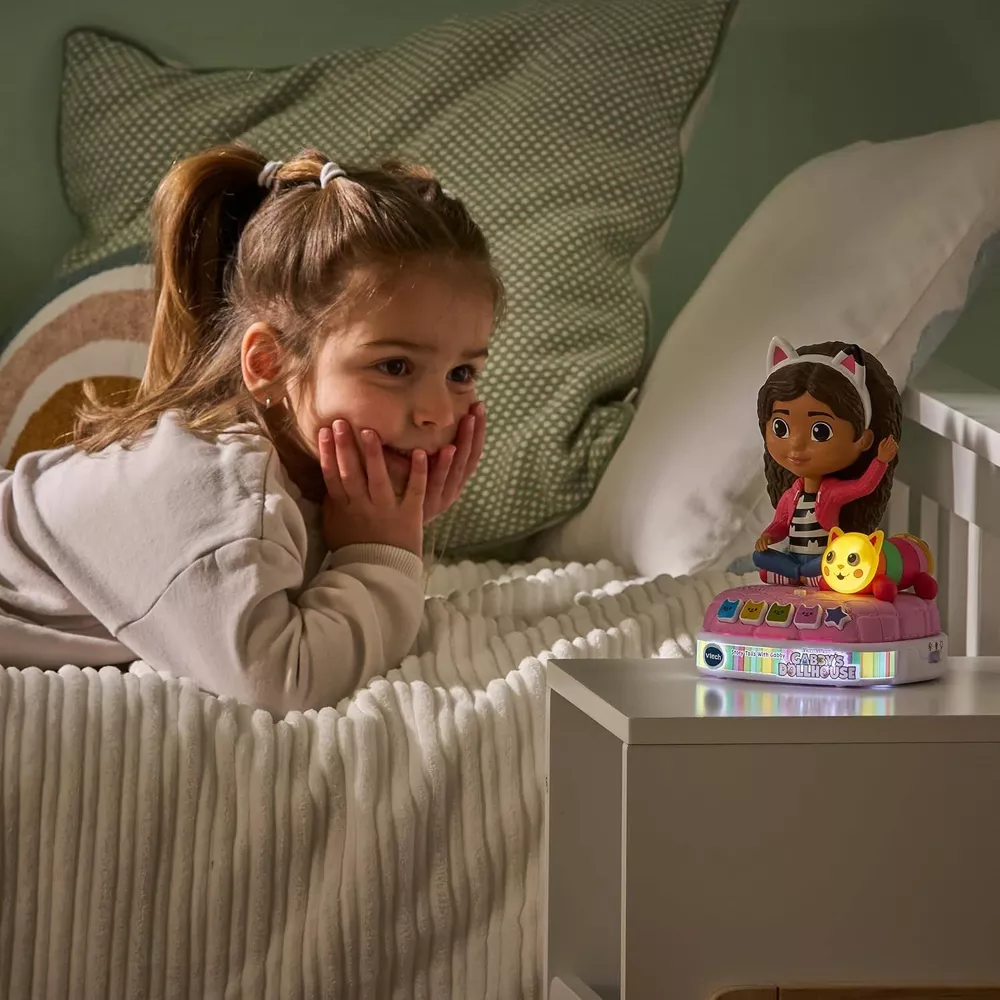 Bambina sdraiata sul letto guarda un giocattolo illuminato con orecchie da gatto.