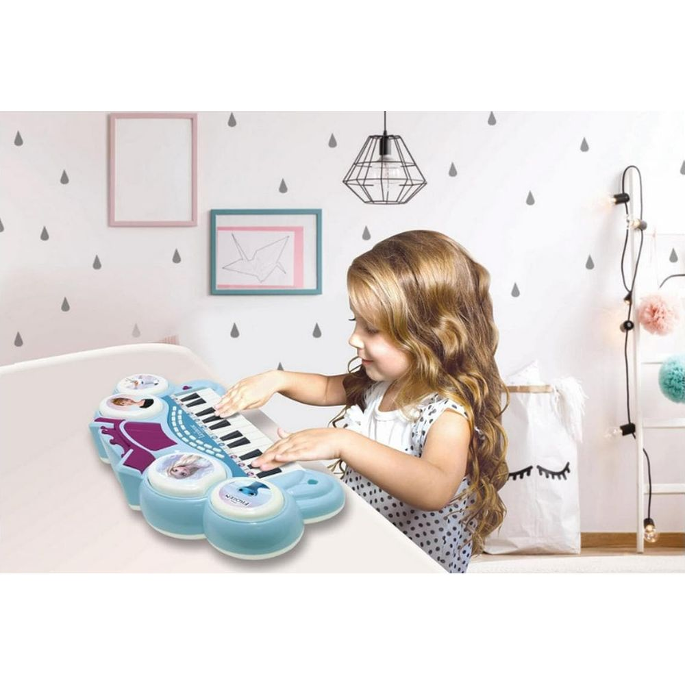 Ein kleines Mädchen spielt auf einem blauen Spielzeugklavier mit Frozen-Motiven.