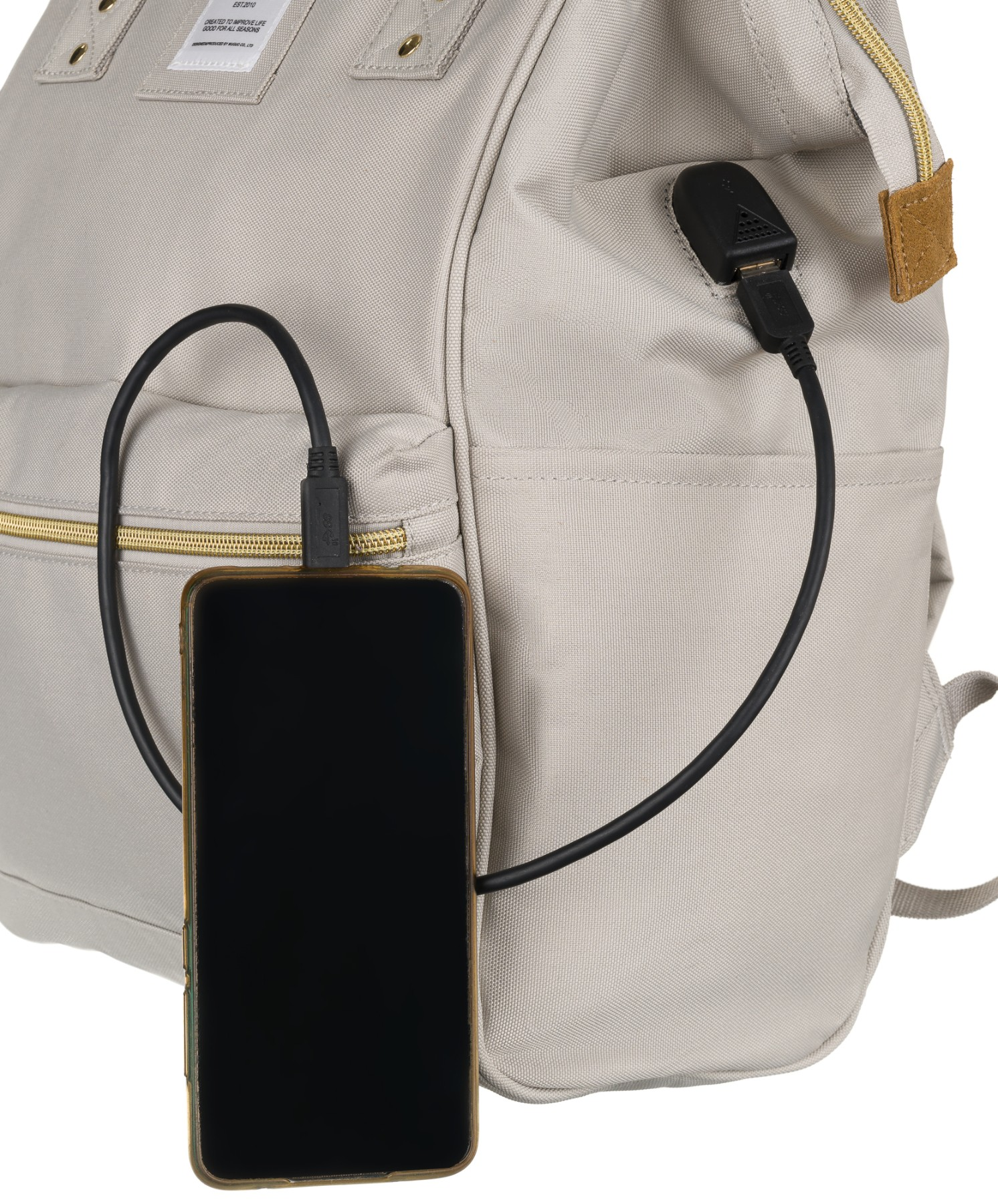 Beżowy plecak z czarnym kablem USB ładującym smartfon. Widoczny port USB.