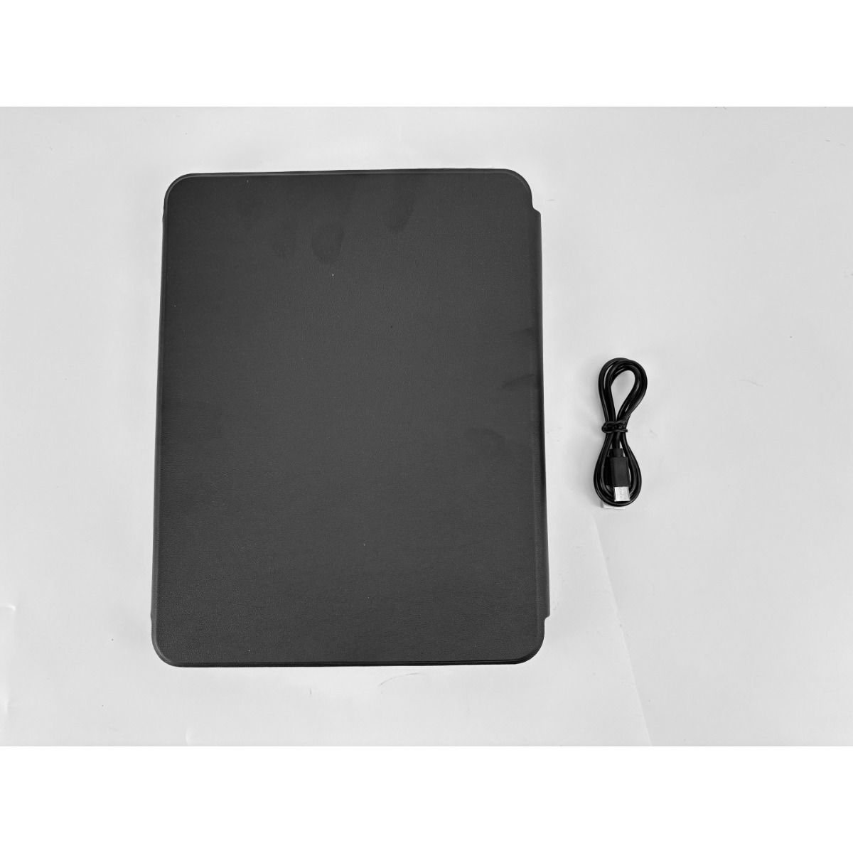 Una custodia nera per tablet è accanto a un cavo di ricarica USB nero su una superficie bianca.