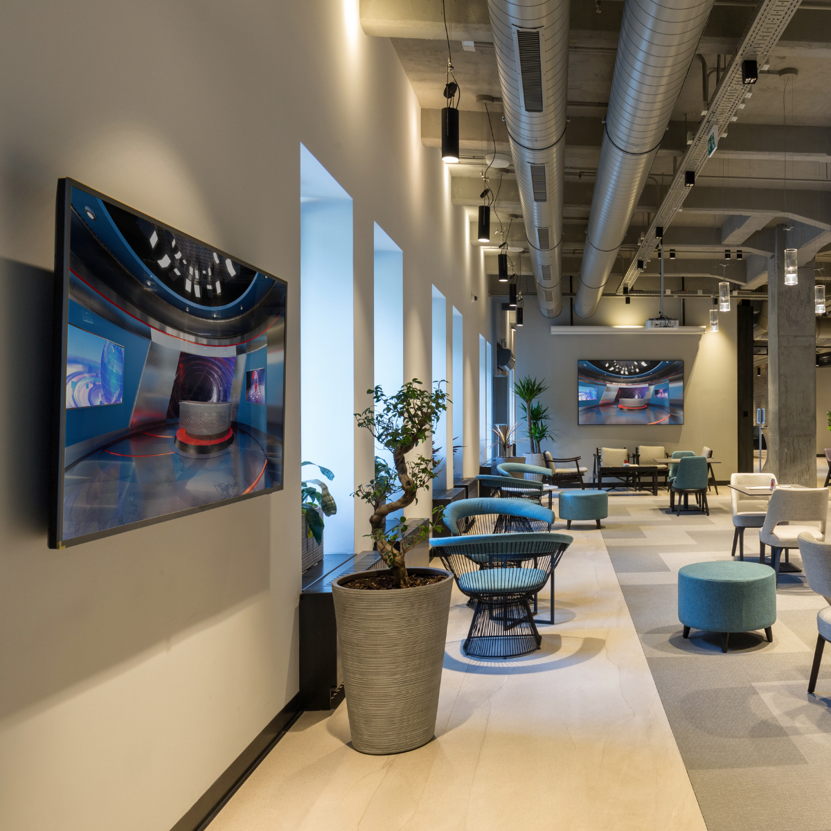 Lounge moderna con grande TV che mostra studio notizie. Sedie blu e piante in vaso.