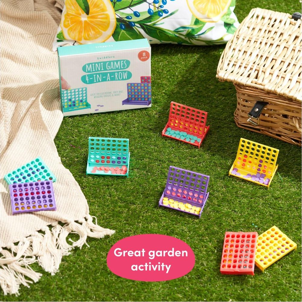 Sei mini giochi Connetti 4 colorati su erba sintetica accanto a una coperta e un cesto da picnic.