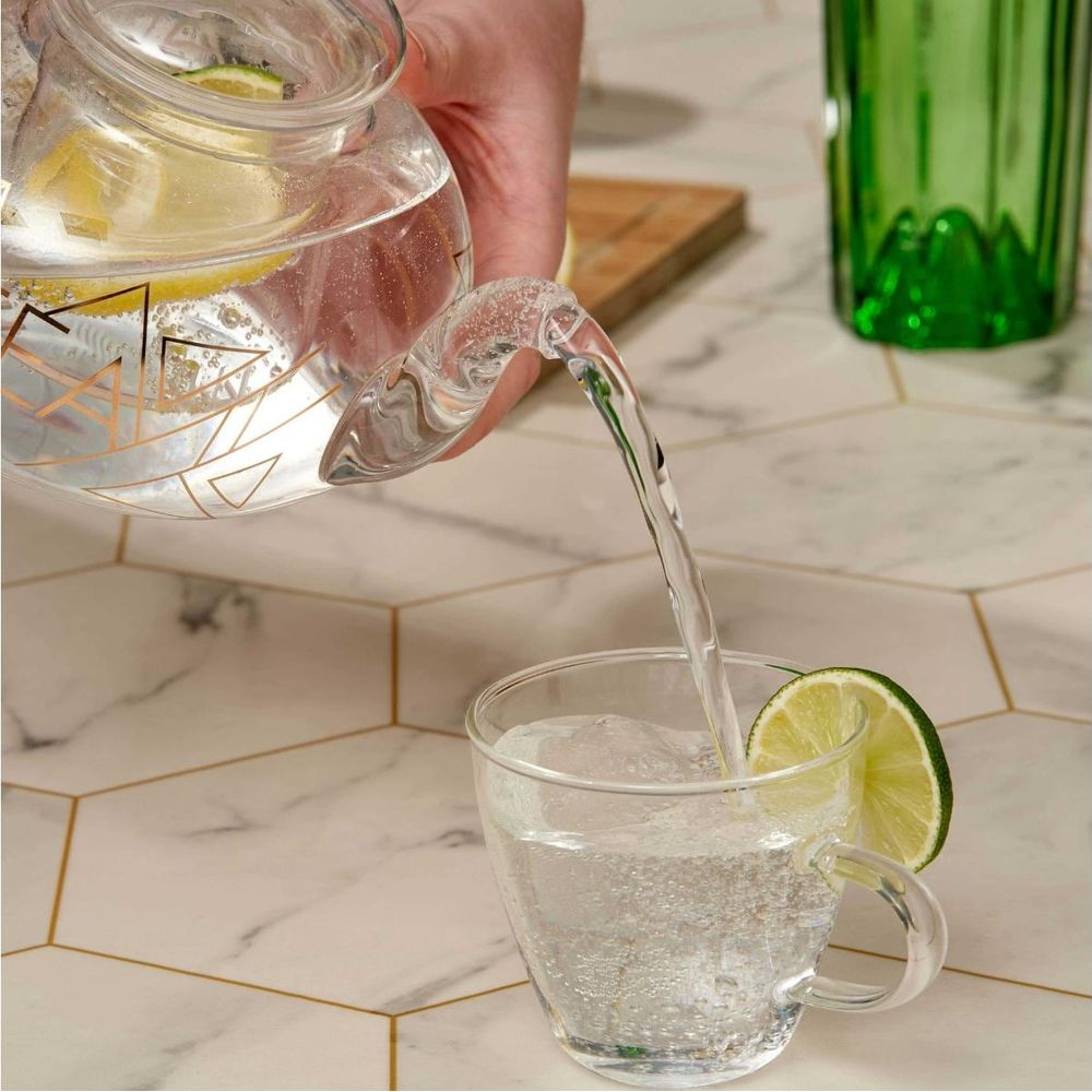 Wasser wird aus einer Karaffe mit Zitronenscheiben in ein Glas gegossen.