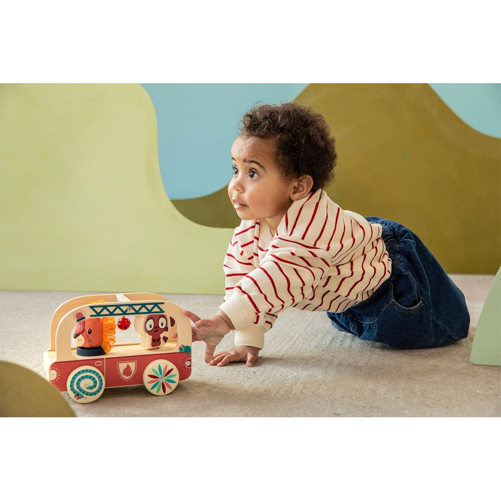 Bambino gattona verso un camion dei pompieri giocattolo in legno con figure di animali.