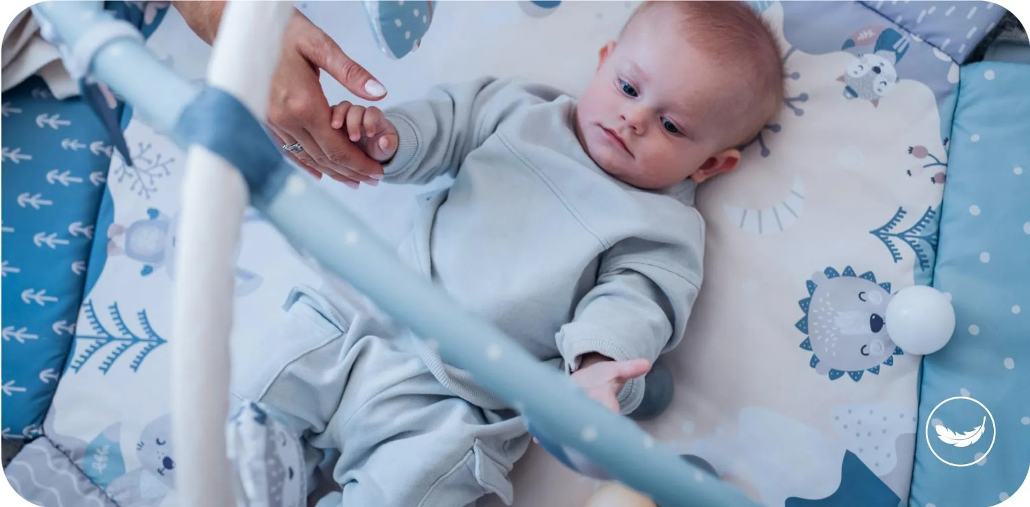 Ein Baby liegt auf einer Spielmatte mit Tiermotiven. Eine Hand hält seine Hand.