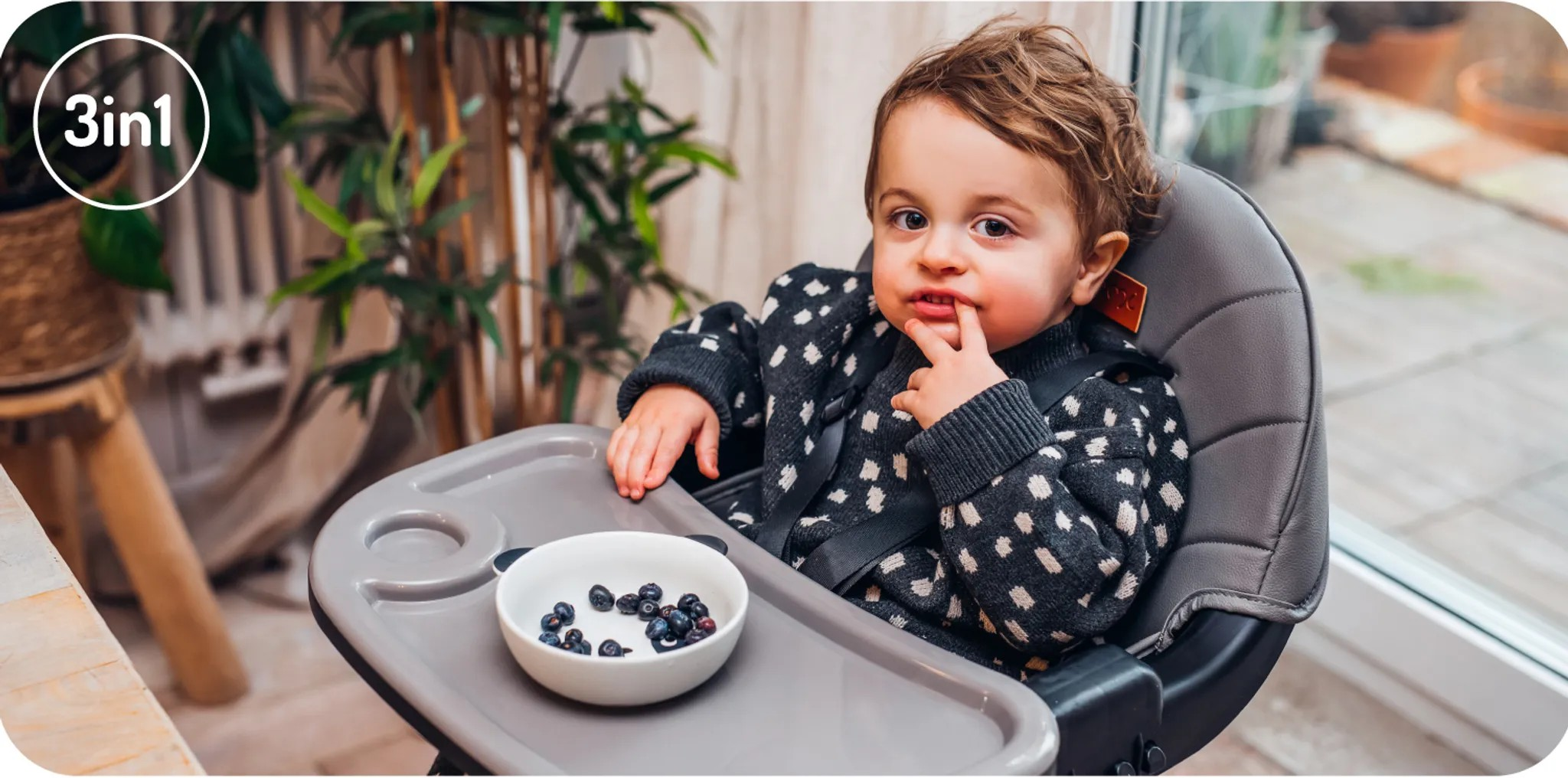 Kleiner Junge im Hochstuhl mit Blaubeeren in einer Schüssel vor ihm.