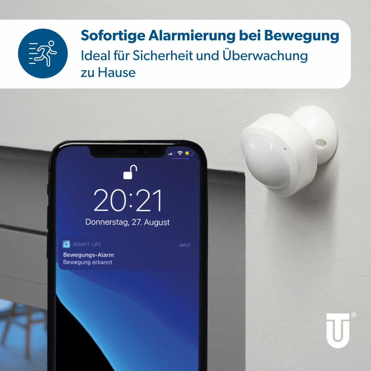 Ein weißer Bewegungsmelder an einer Wand neben einem Smartphone mit Alarmmeldung.