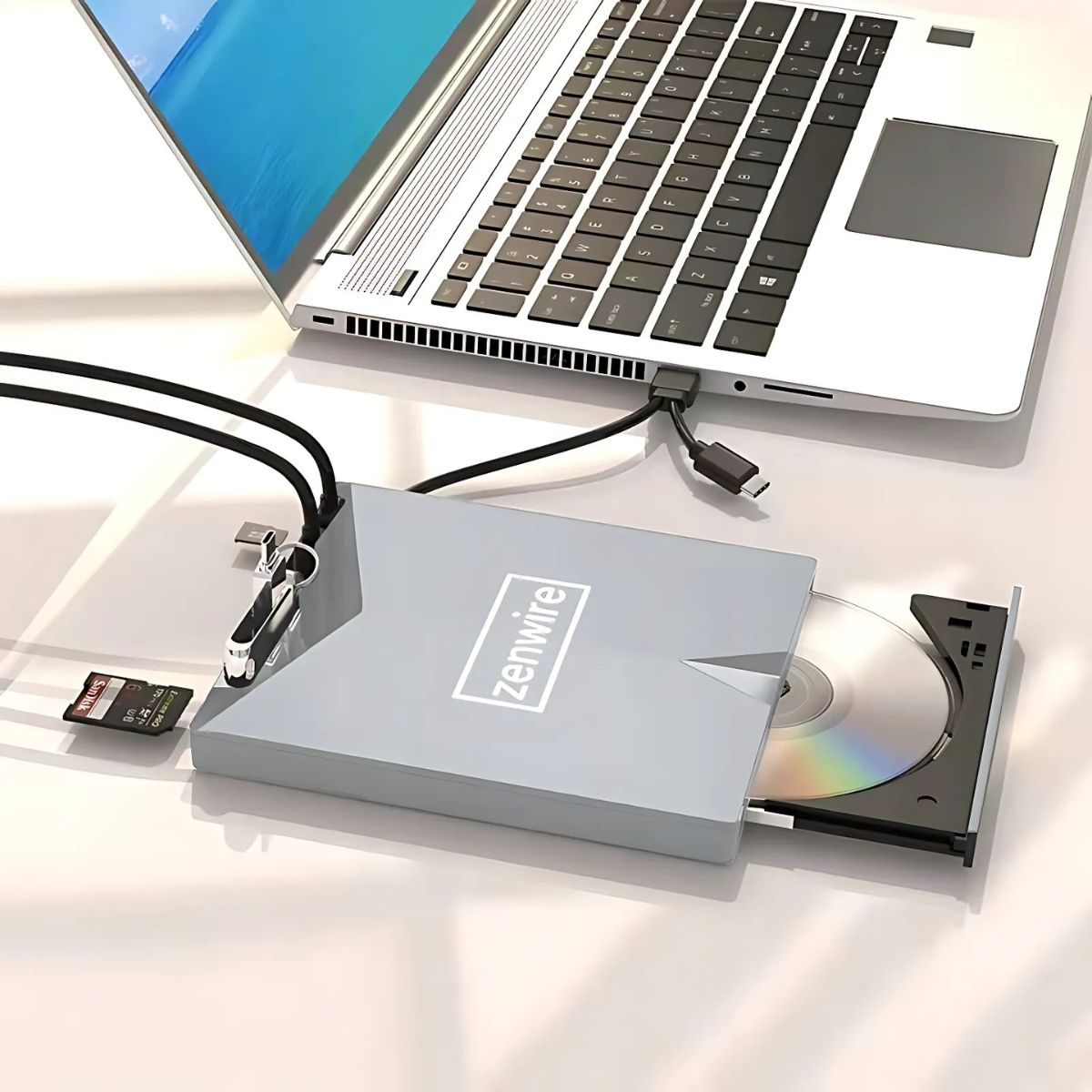 Srebrny laptop łączy się z szarym napędem CD/DVD Zenwire przez kabel USB-C. W pobliżu znajduje się karta SD.